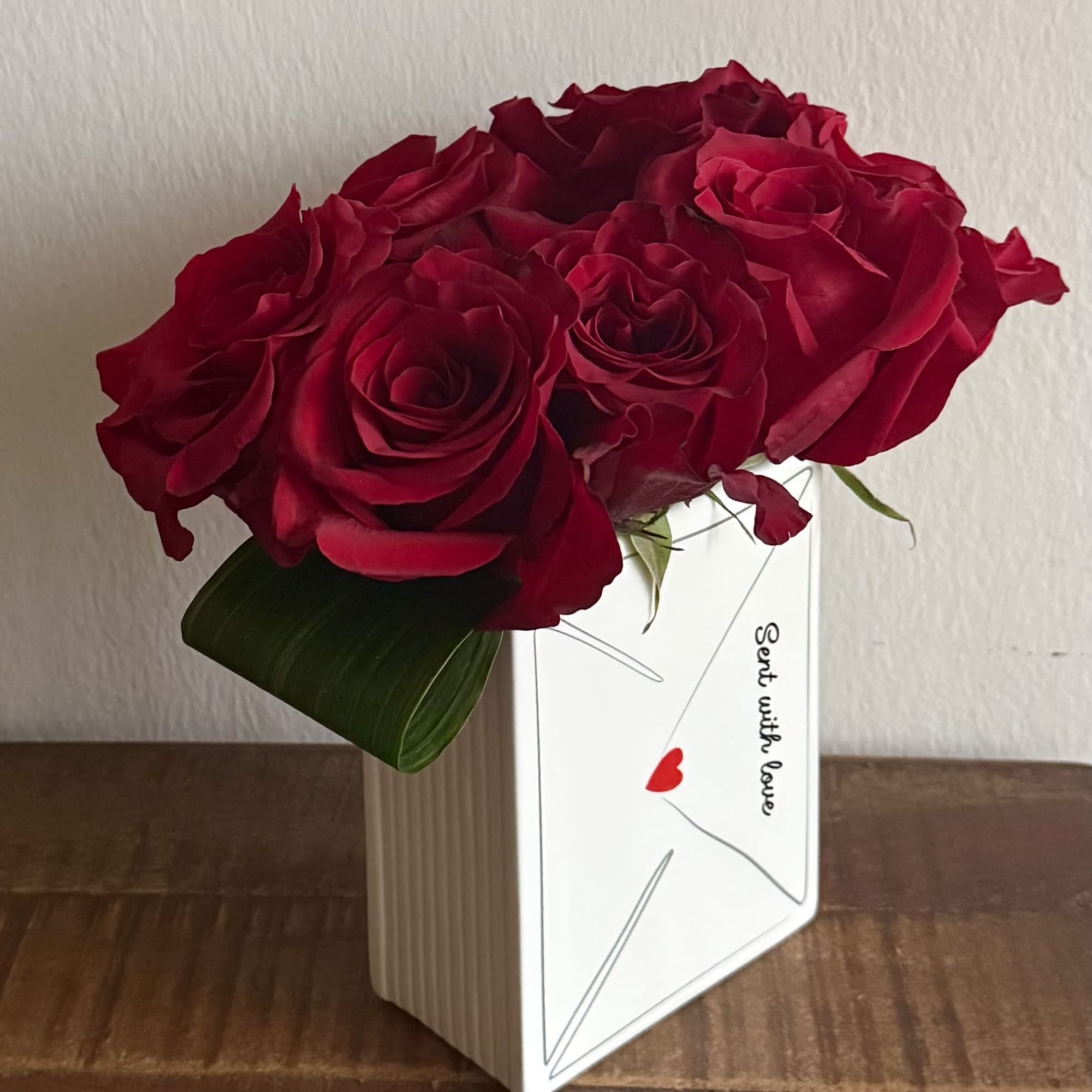 Red roses arranged in a white envelope-style vase with a love note