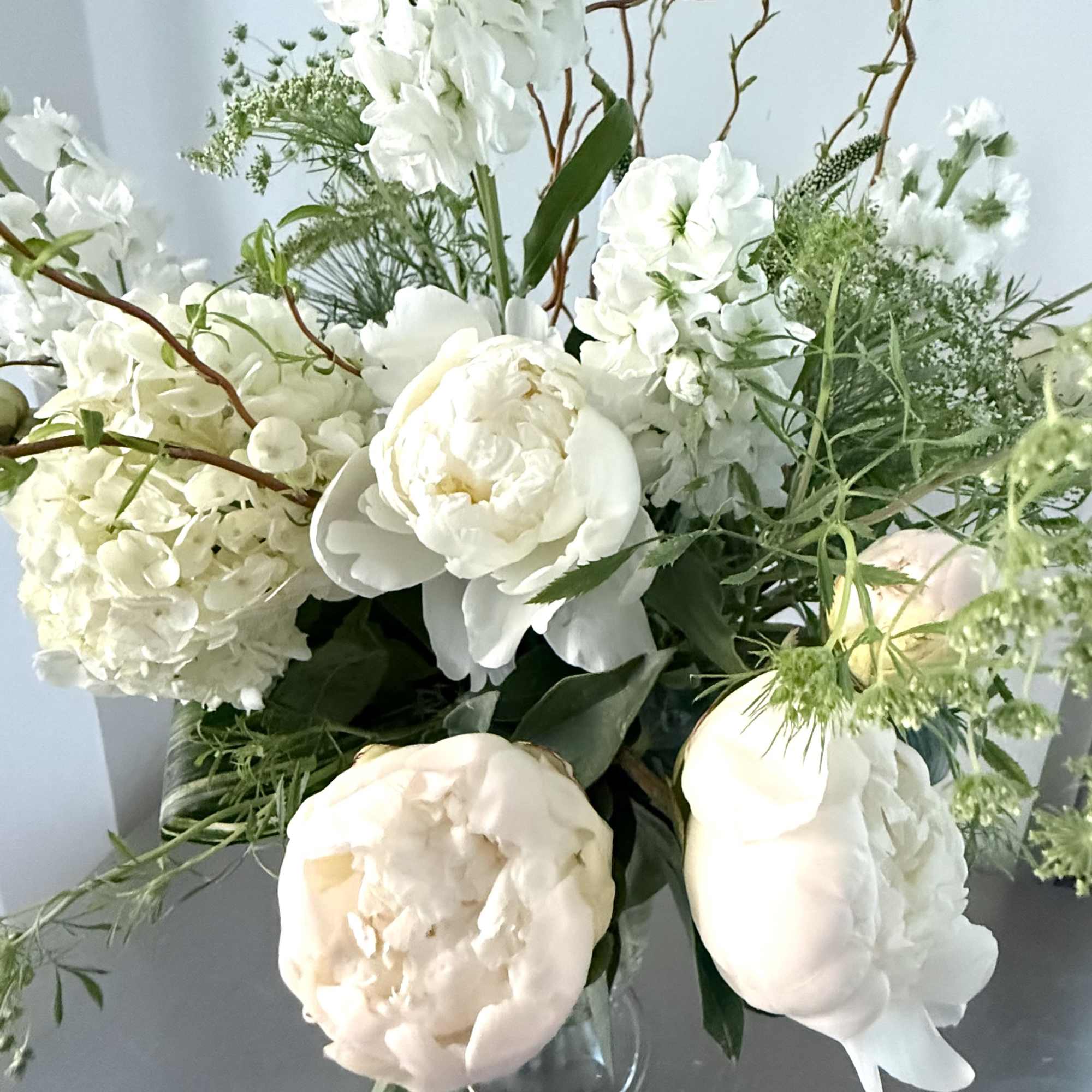 White floral bouquet with peonies, hydrangeas, and greenery in a glass vase
