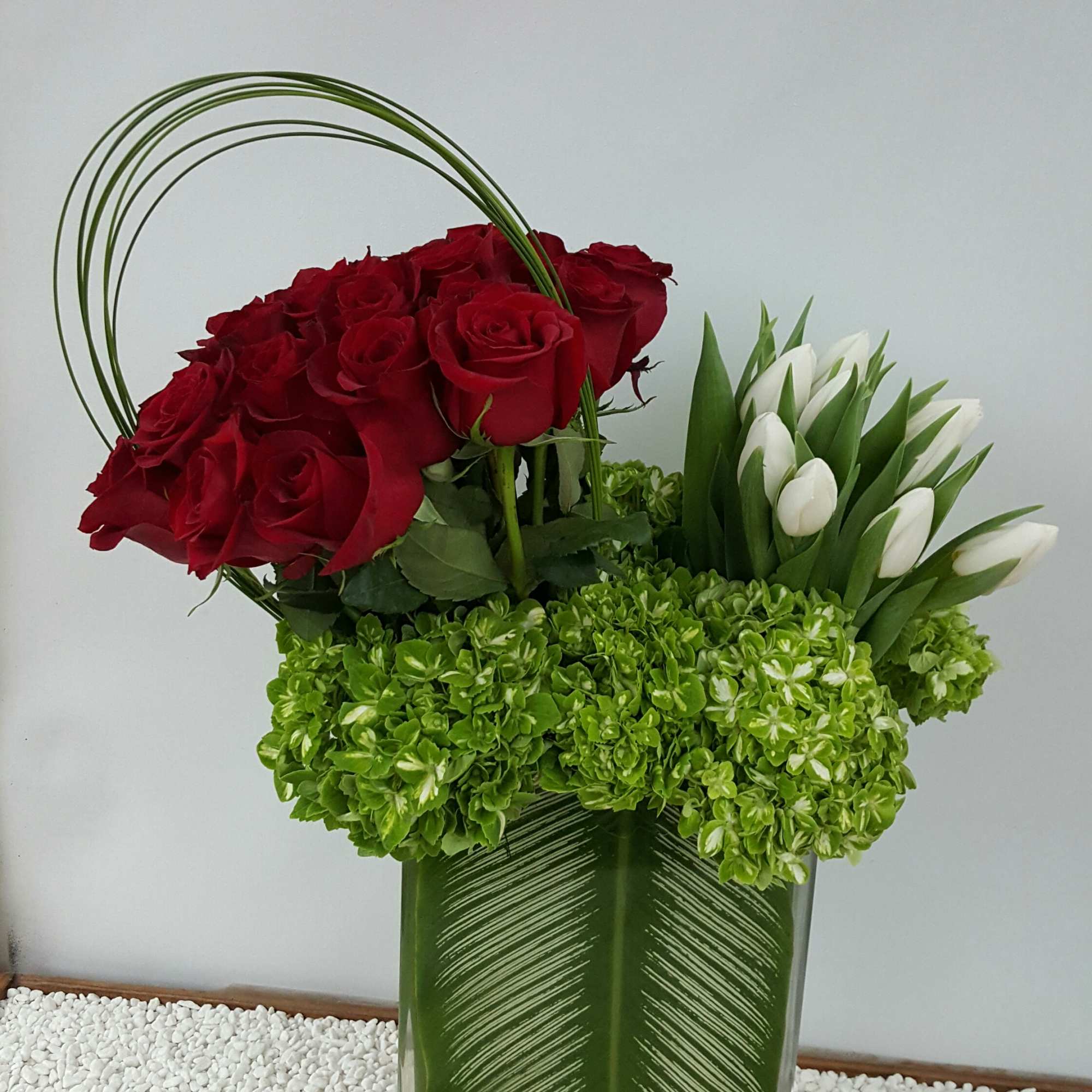 Red roses and white tulips in a green glass vase with a loose rose on the side