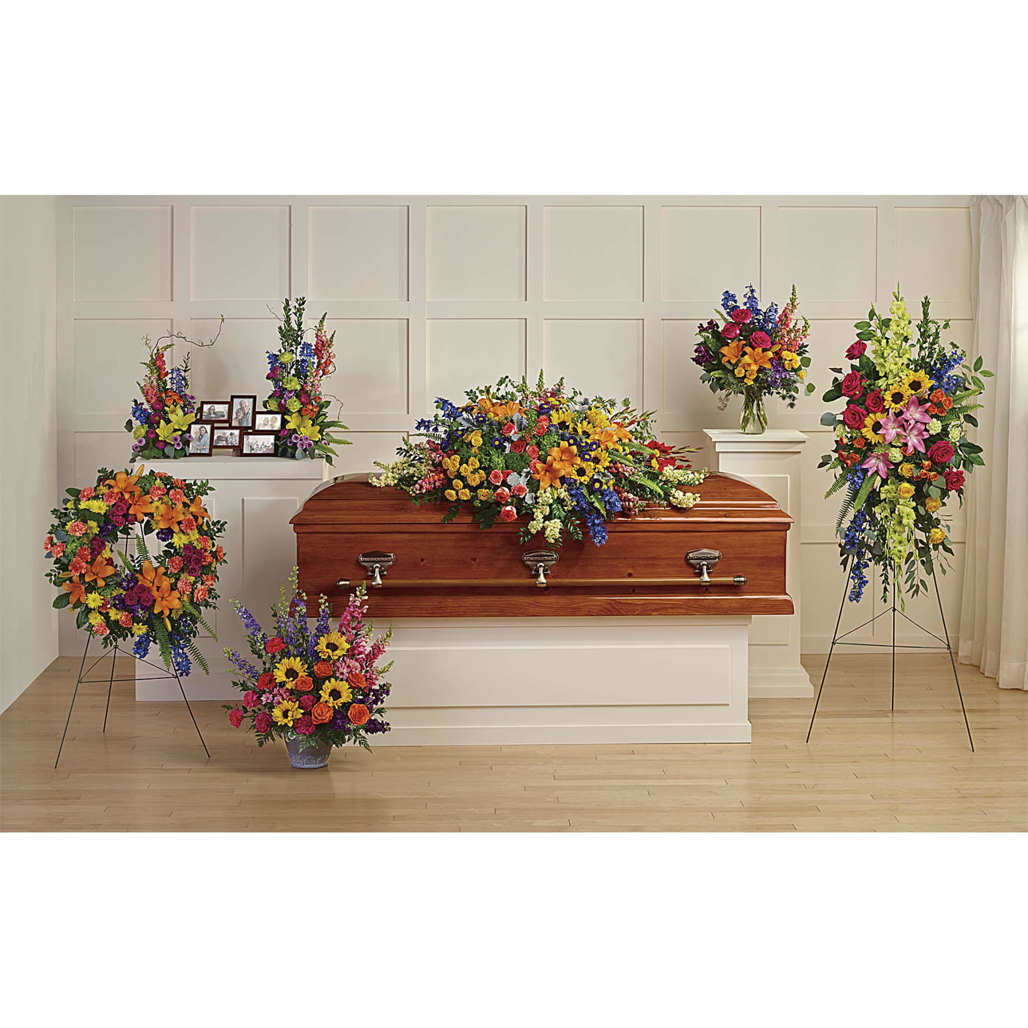 Colorful funeral floral set with casket spray, standing sprays, wreath, and vase around a wooden casket