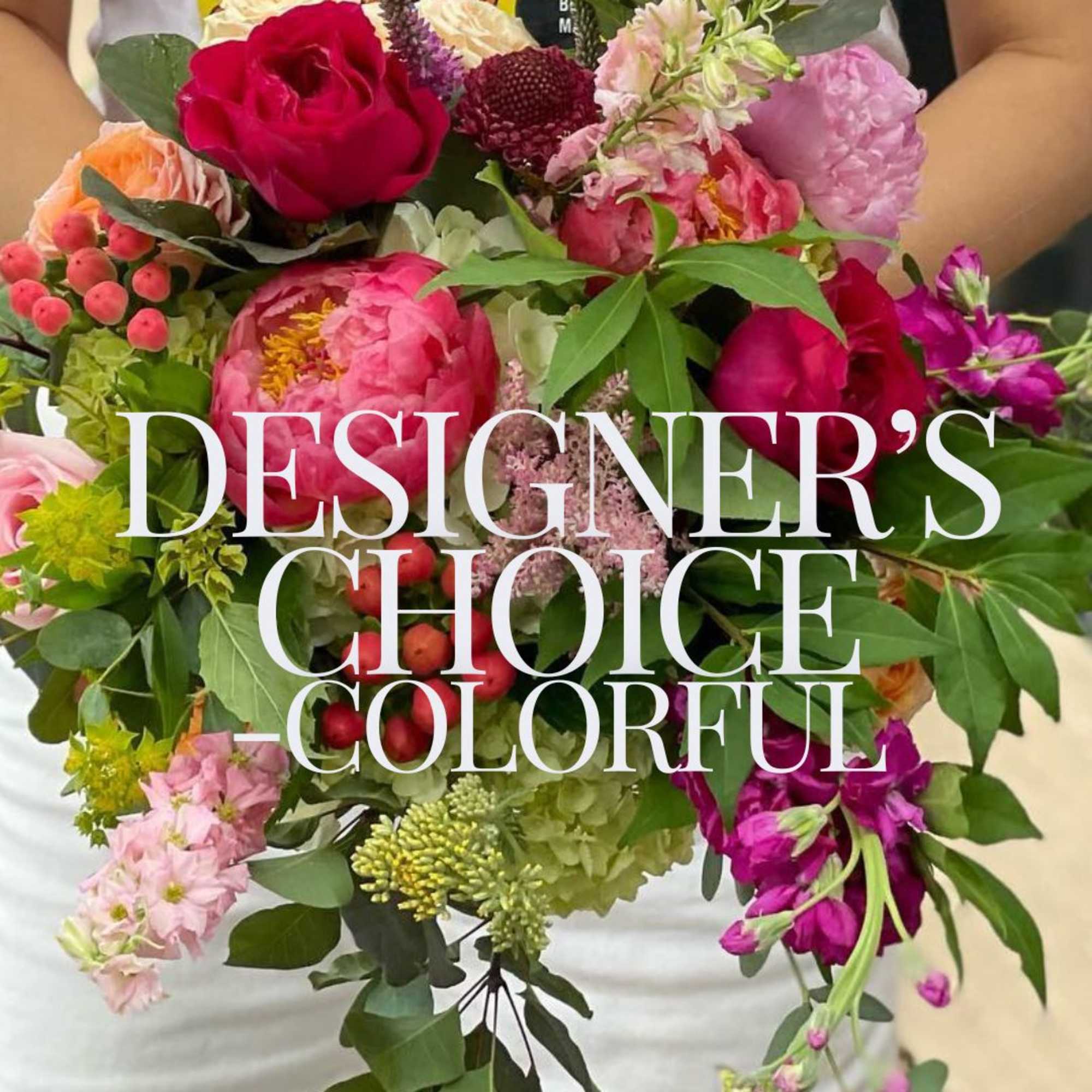 Colorful mixed bouquet of pink peonies, roses, and other bright blooms held in both hands