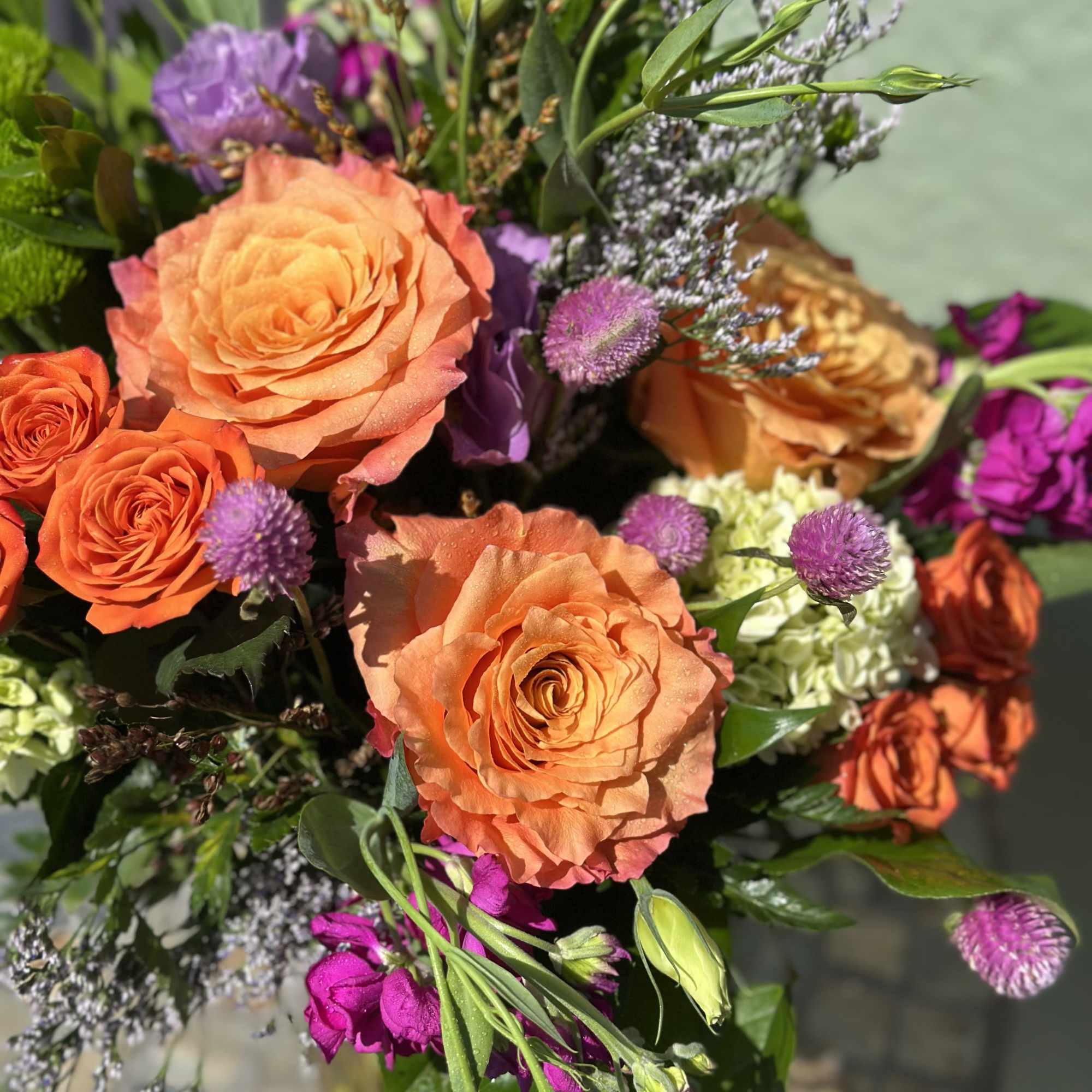 Bright bouquet of orange roses, purple blooms, and mixed flowers in a vase