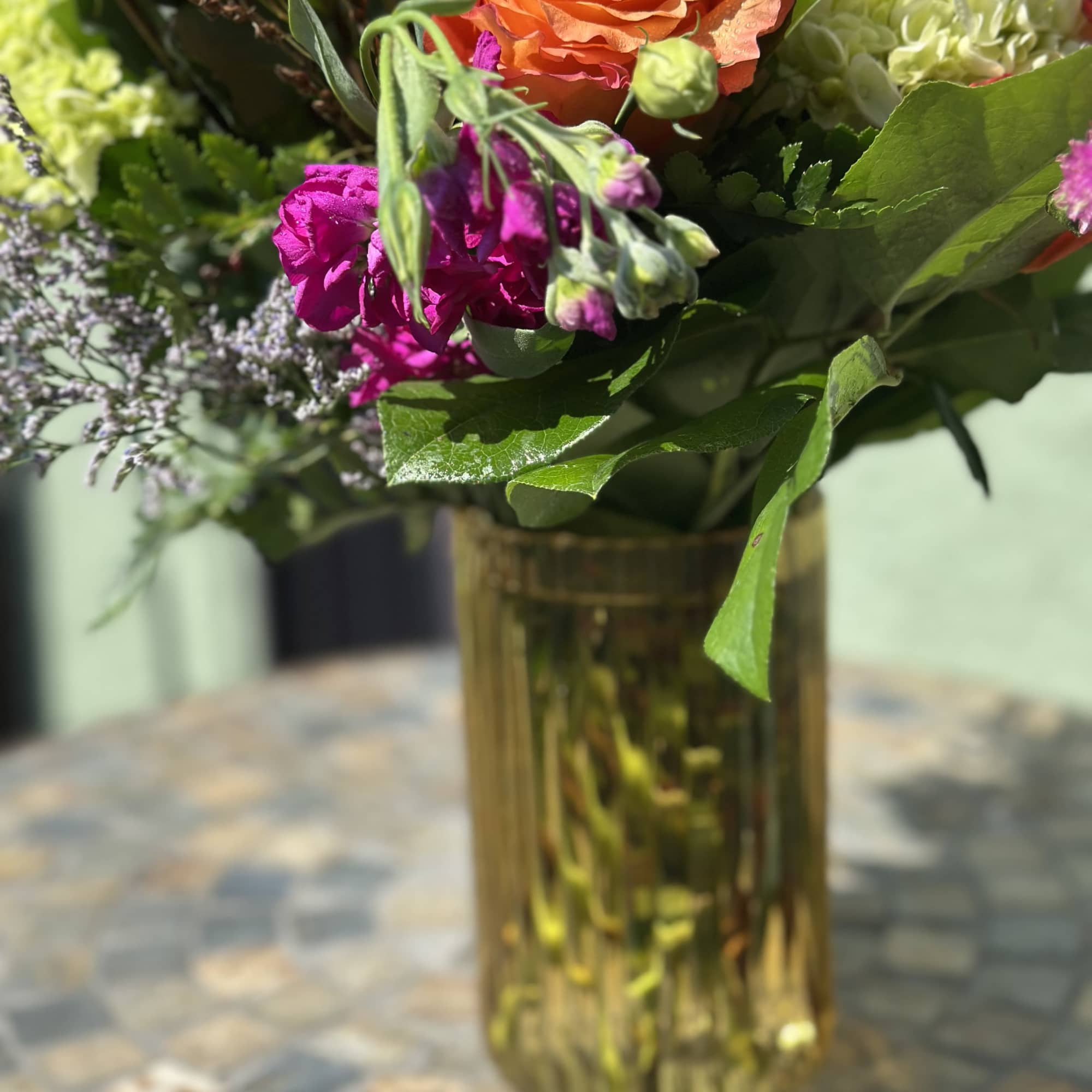 Bright mixed bouquet with orange roses, green hydrangea, and fuchsia blooms in a gold glass vase