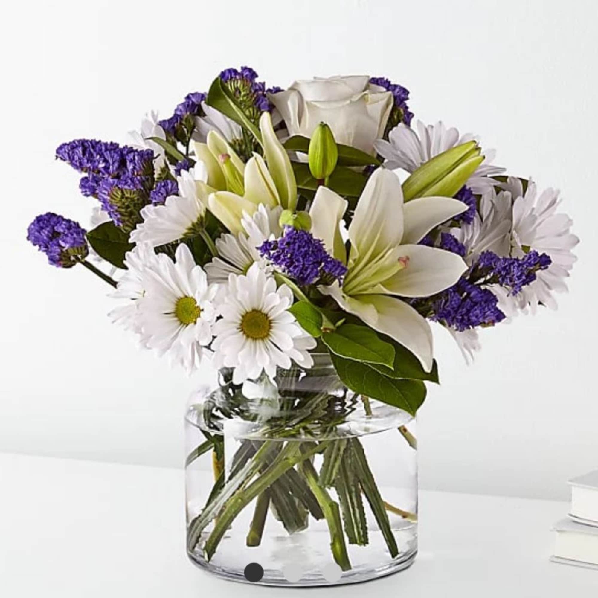 White lilies and daisies with purple filler in a clear glass vase
