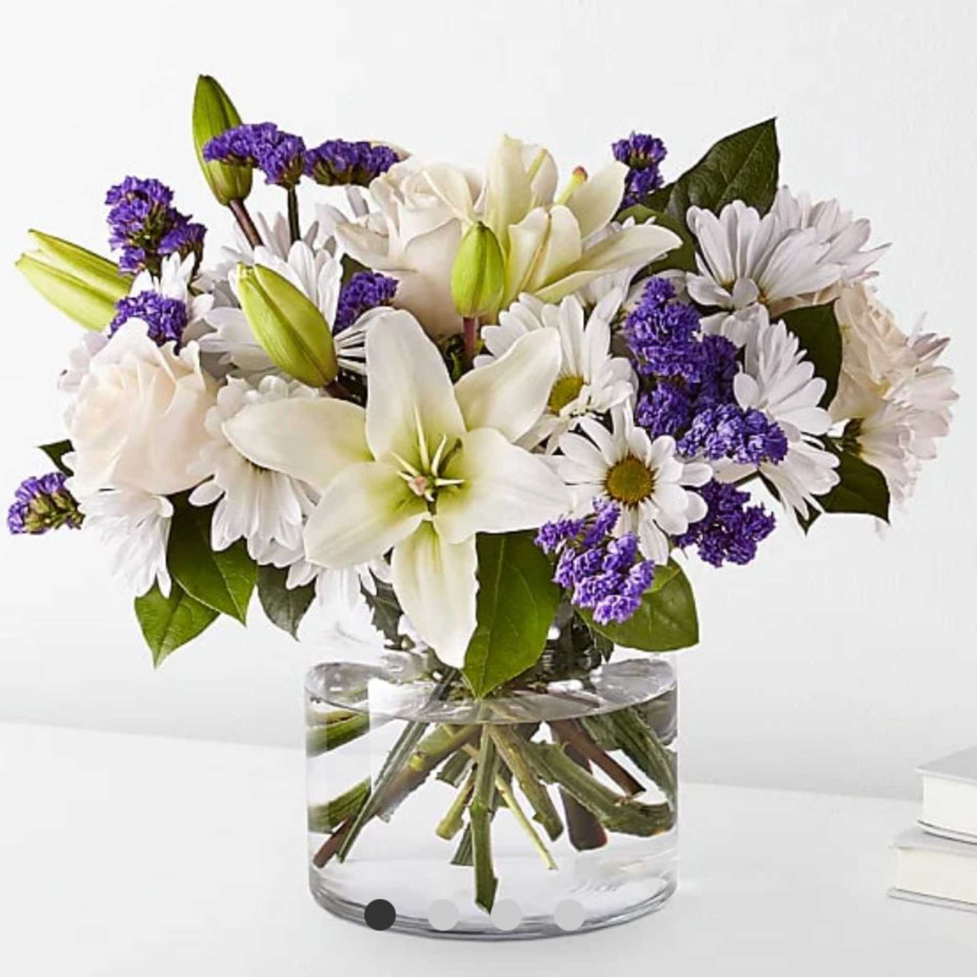 White lilies and daisies with purple filler in a clear glass vase