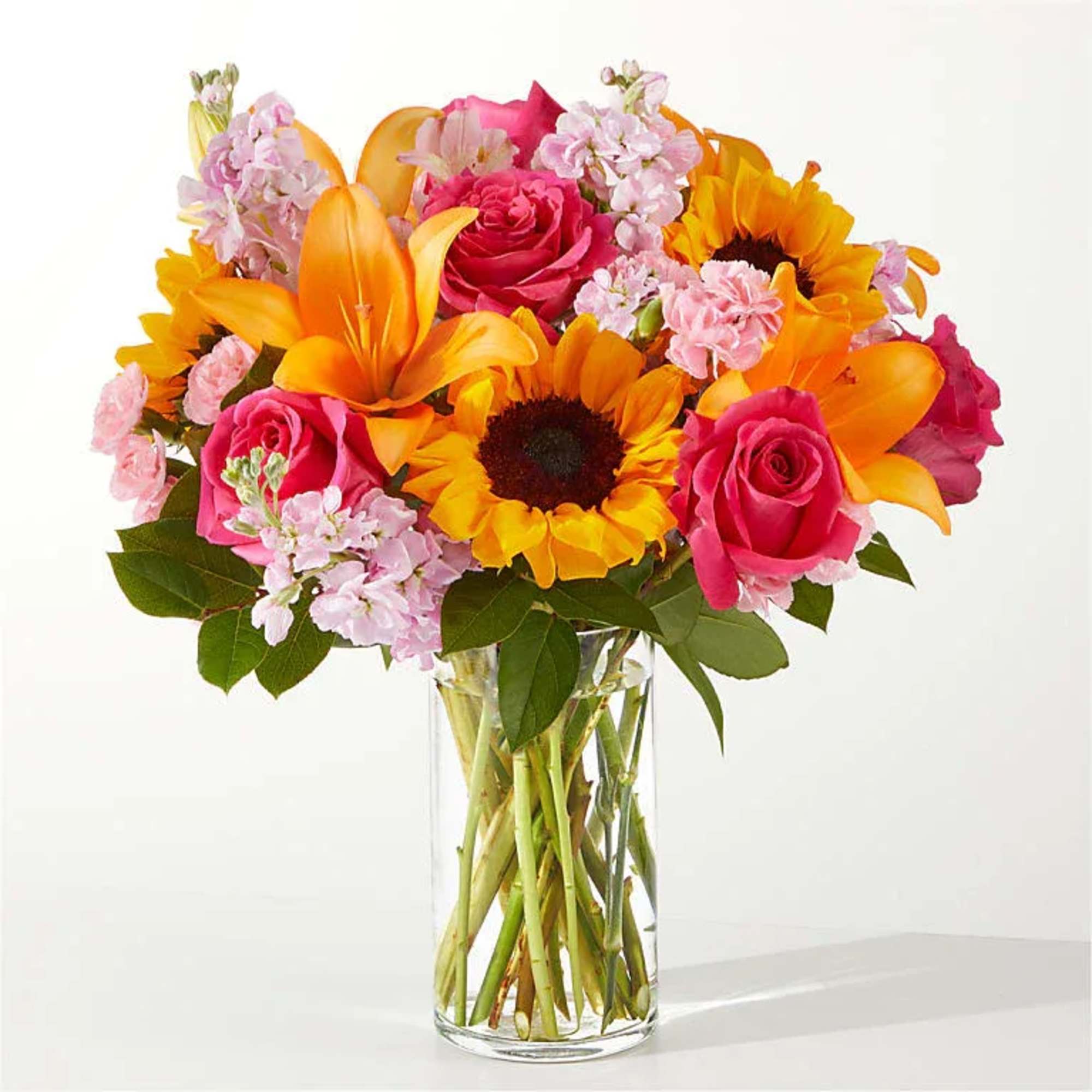 Bouquet of pink roses, sunflowers, and orange lilies in a glass vase