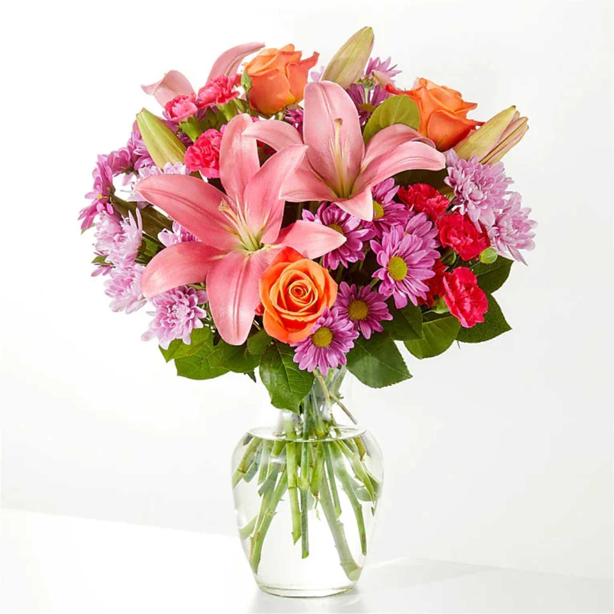 Bouquet of pink lilies, orange roses, and purple daisies in a clear glass vase