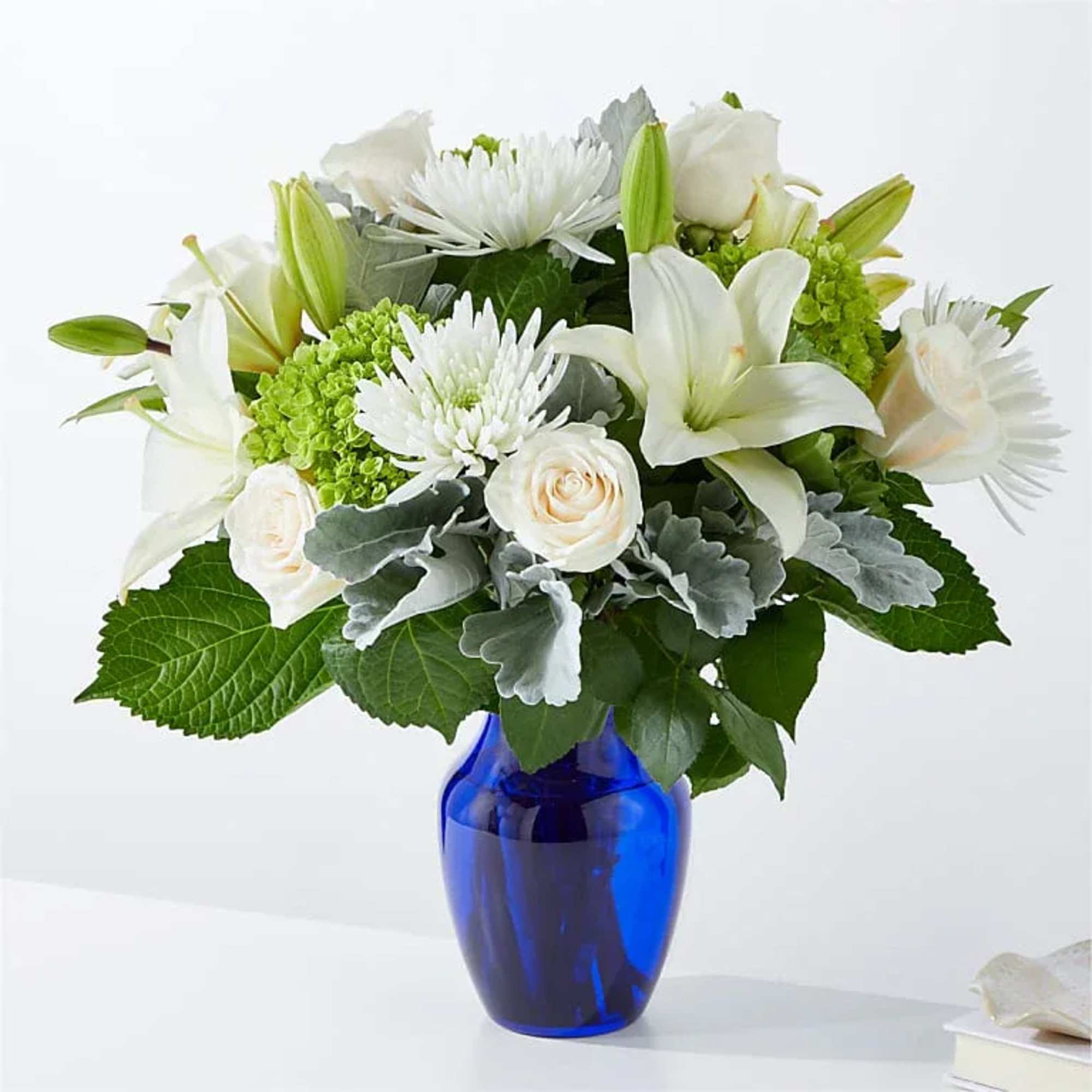 White lilies and roses arranged in a blue glass vase