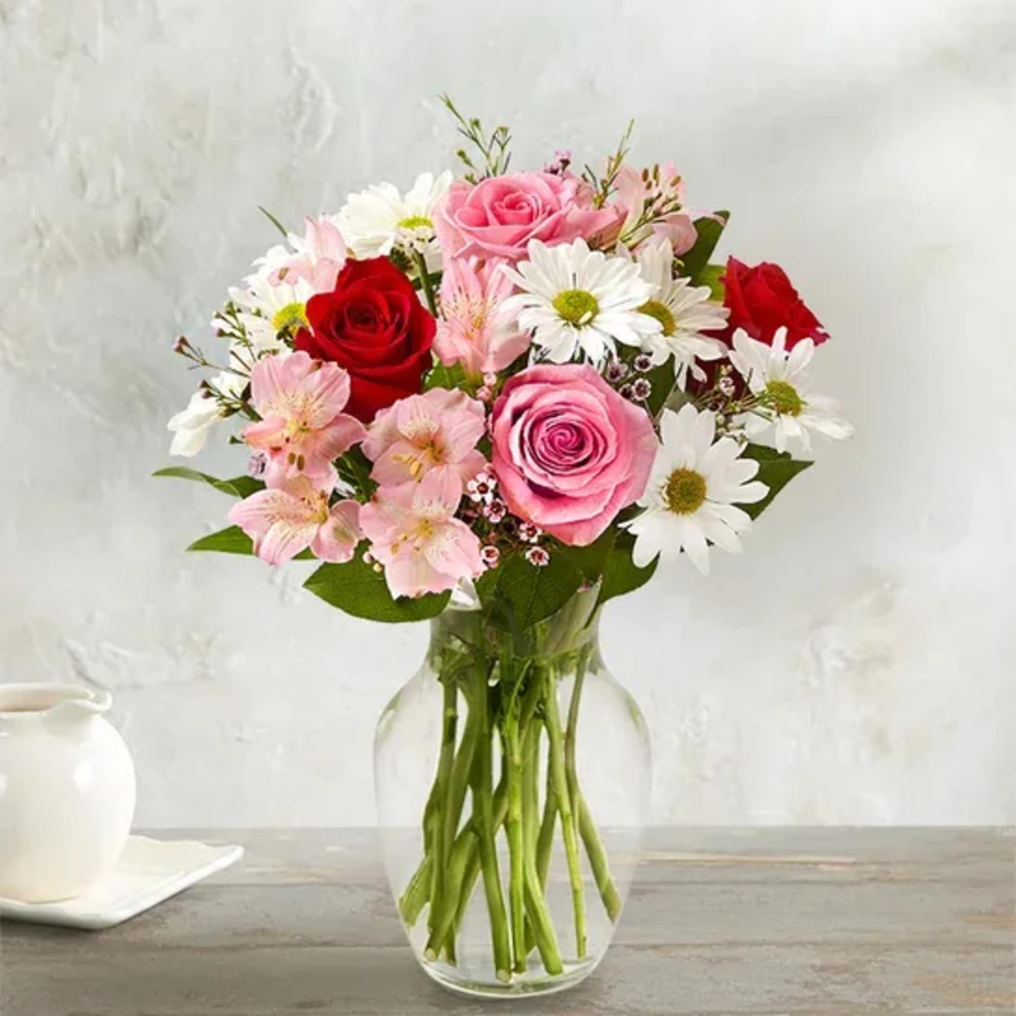 Pink and red roses with white daisies in a clear glass vase