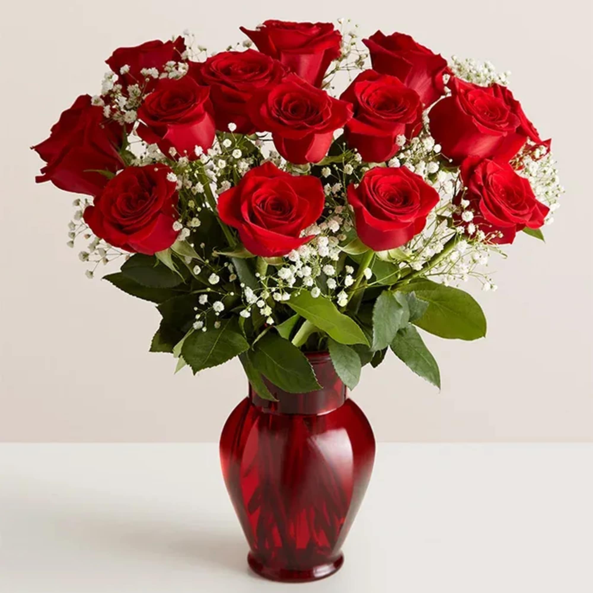 Red roses arranged in a red glass vase with white baby's breath