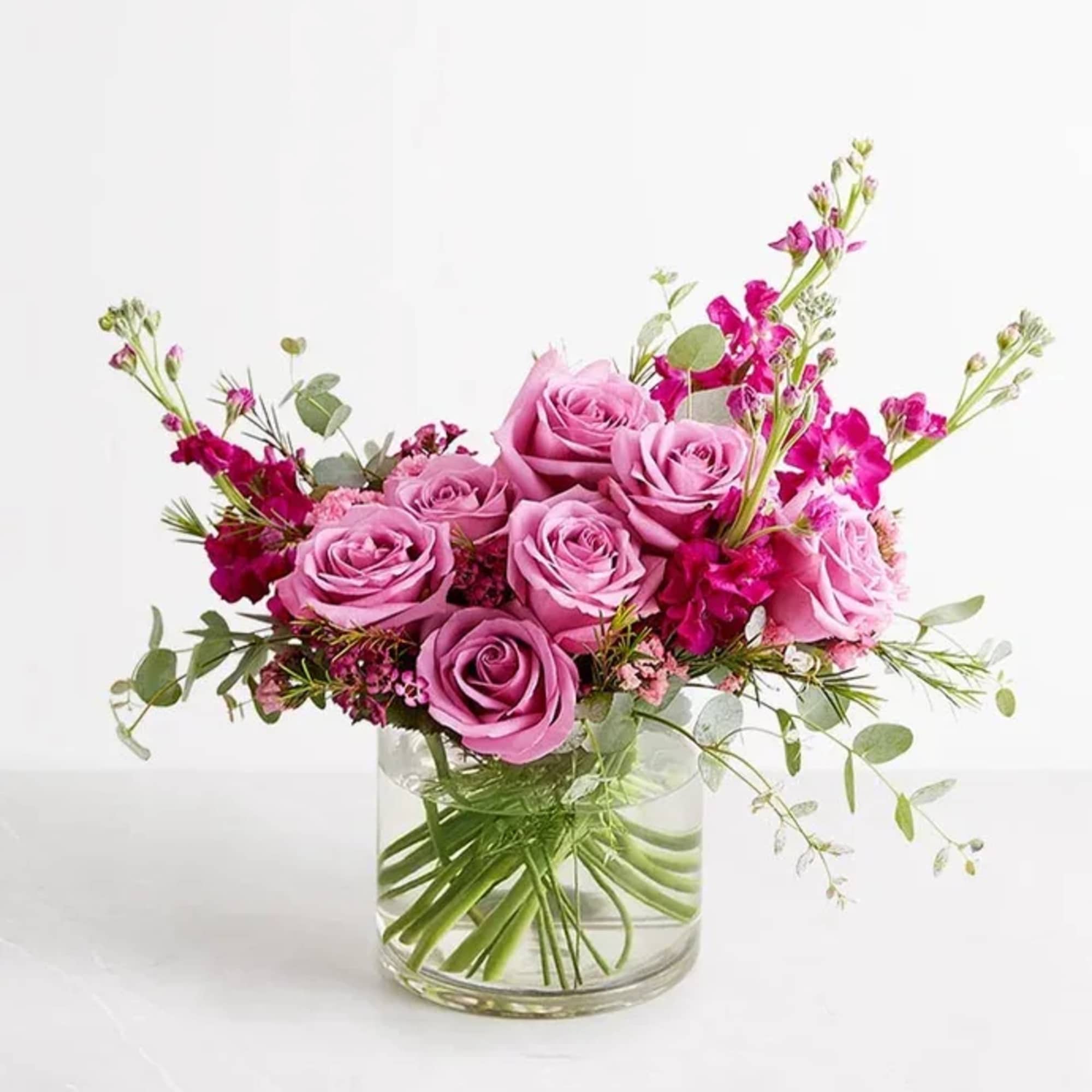 Pink roses and magenta flowers arranged in a clear glass vase