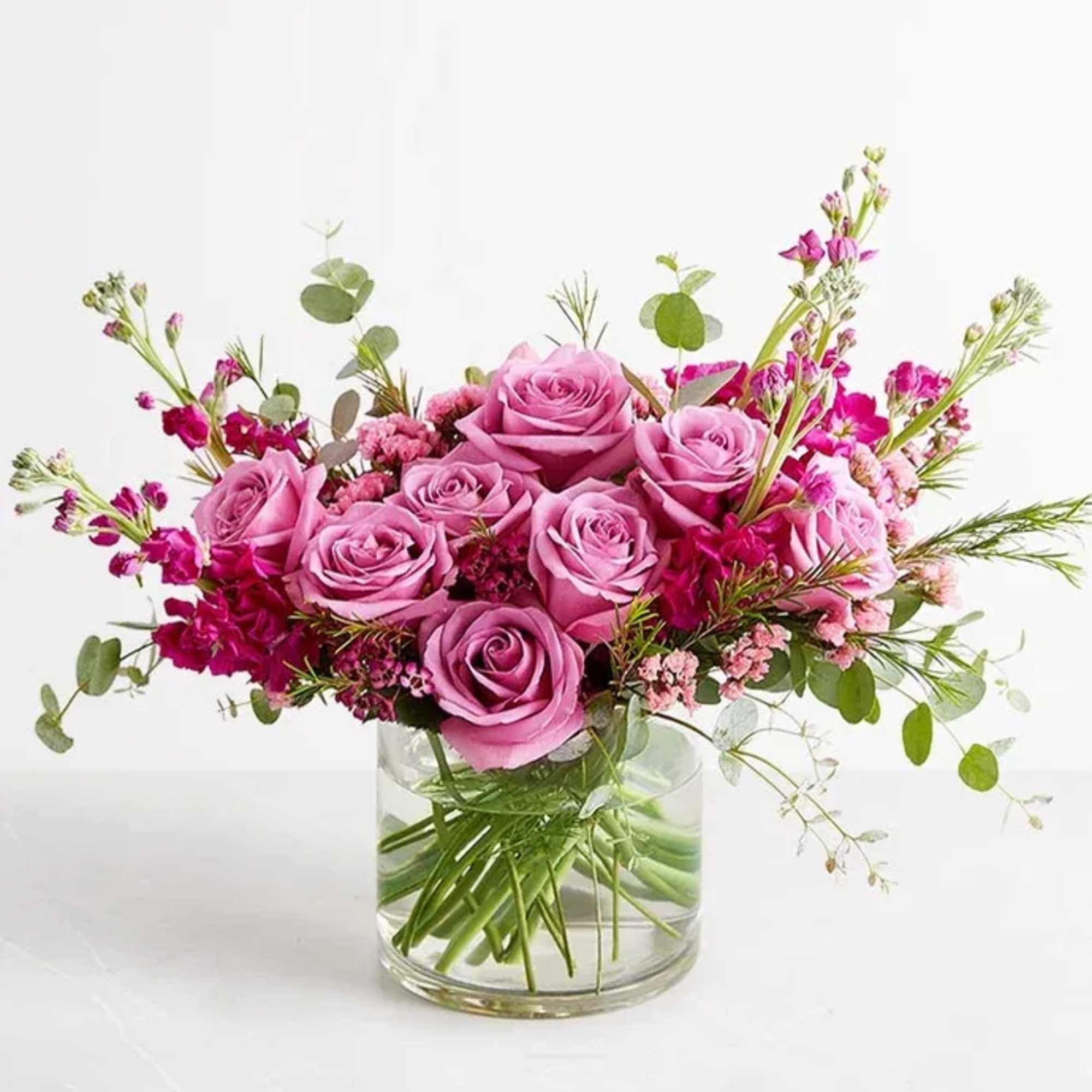 Pink roses arranged in a clear glass vase with small magenta blooms