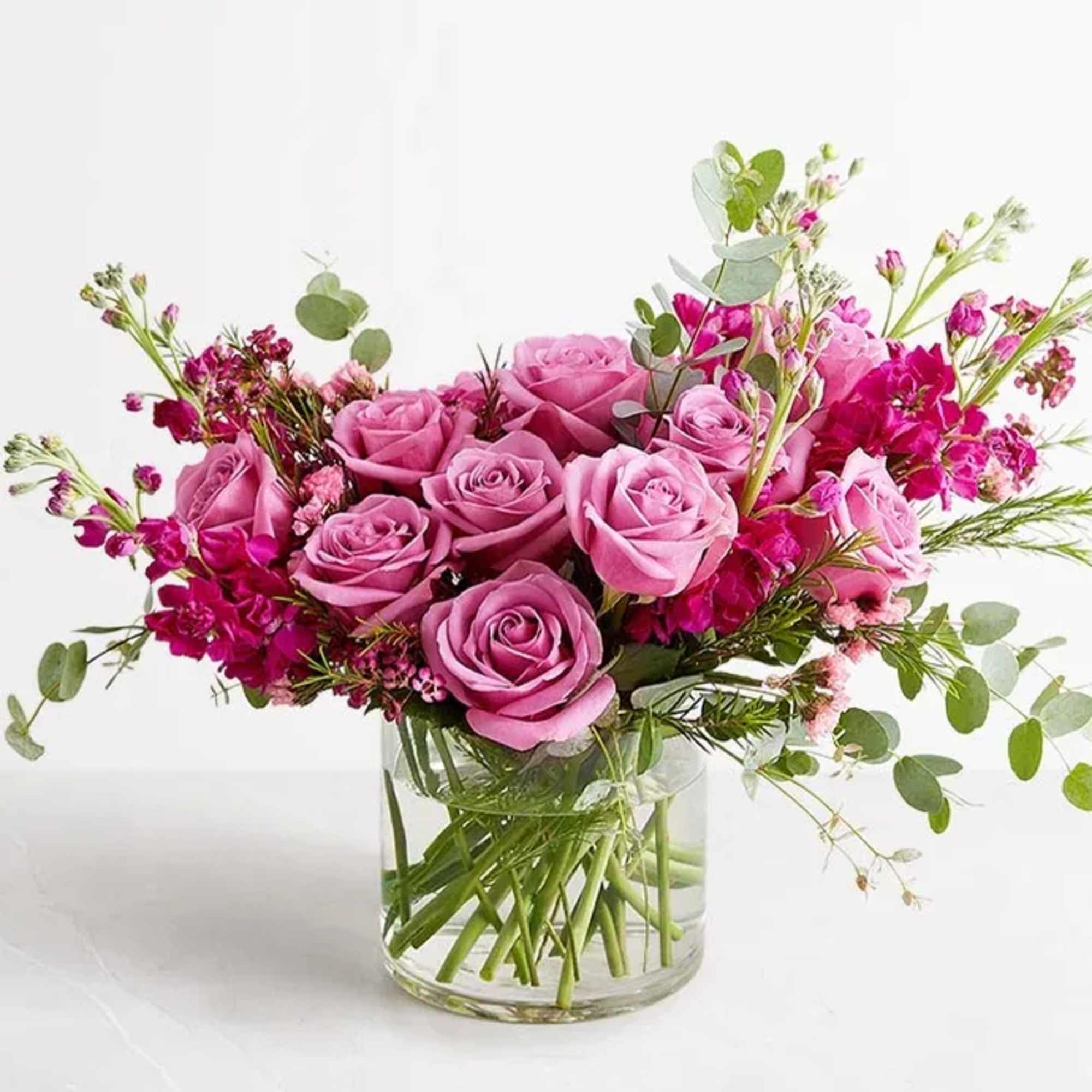 Pink roses and magenta flowers arranged in a clear glass vase