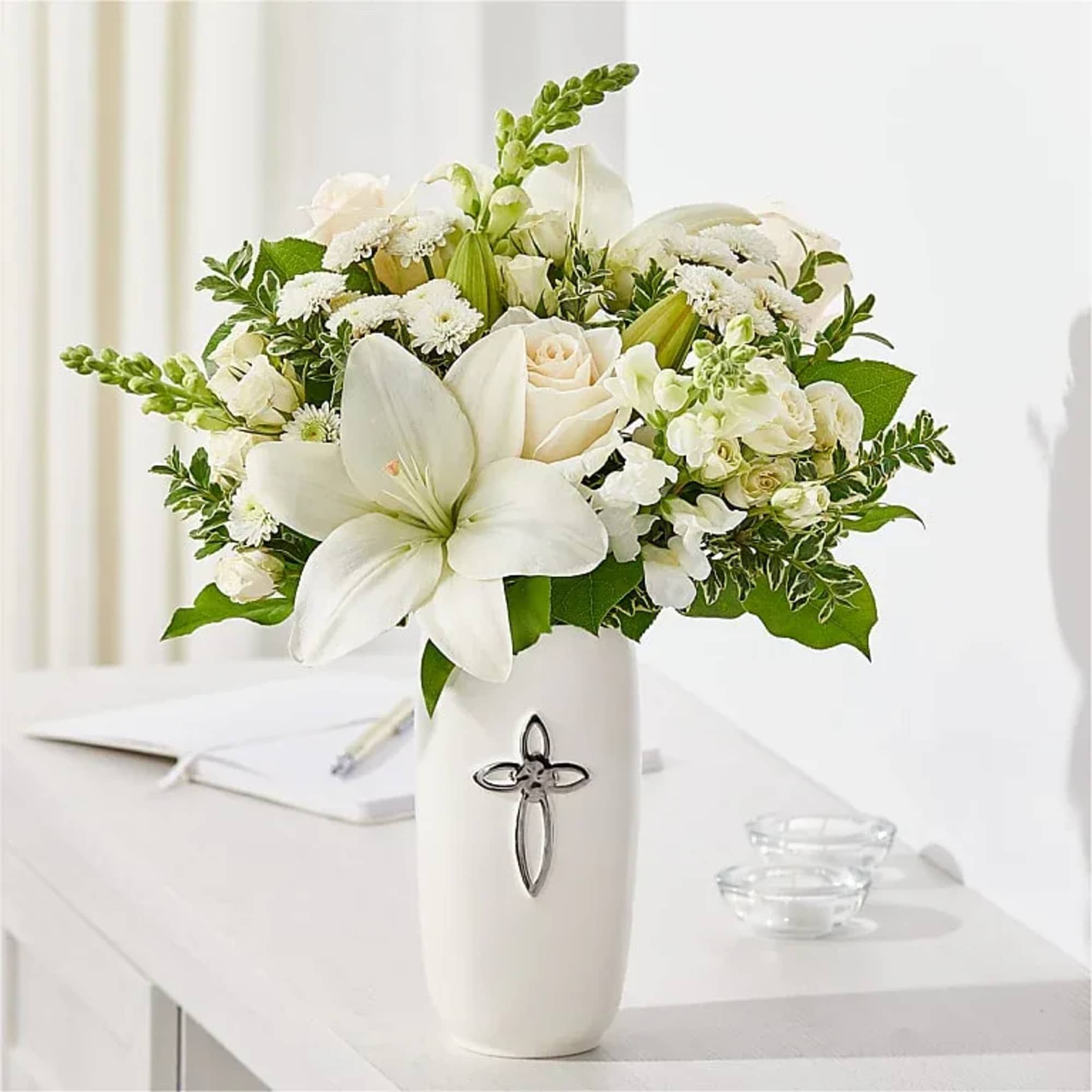 White floral arrangement in a tall vase with a cross emblem