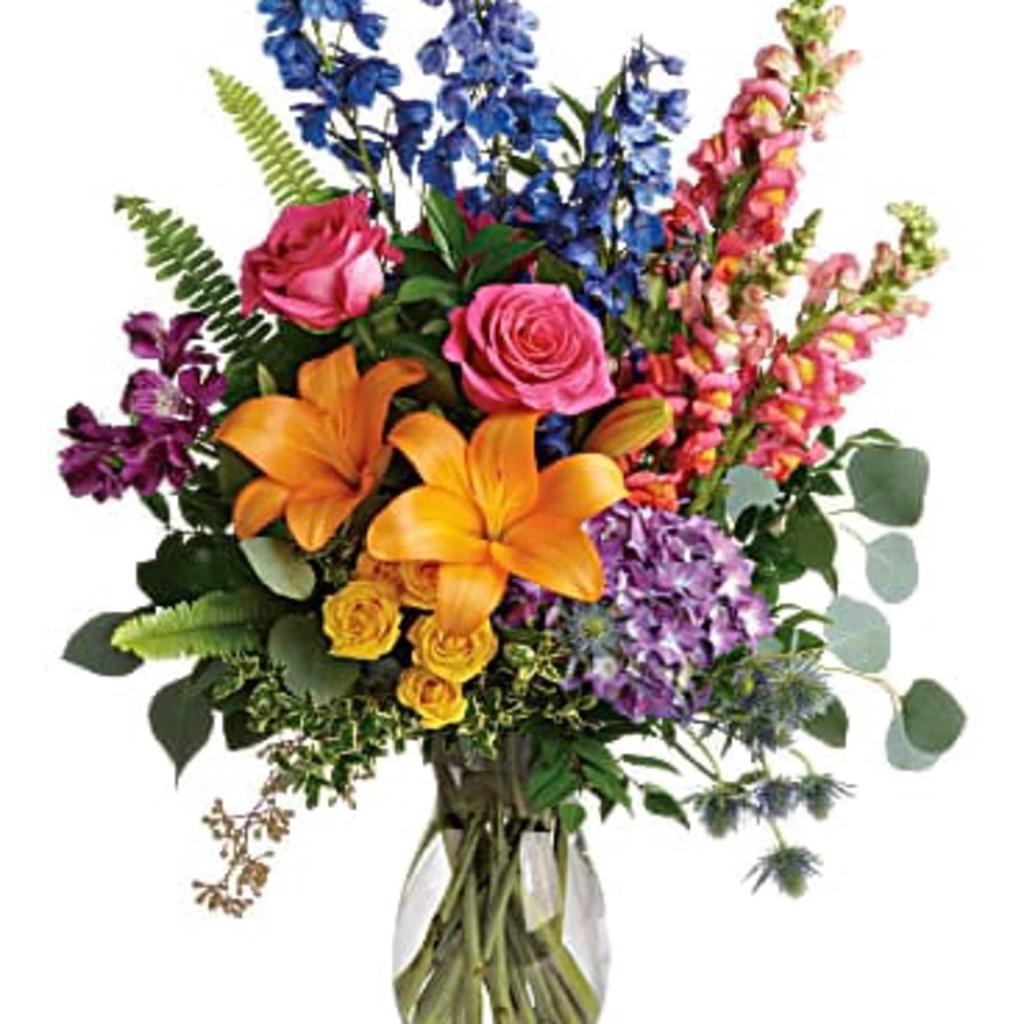 Colorful mixed bouquet in a clear glass vase with lilies, roses, and tall blue blooms
