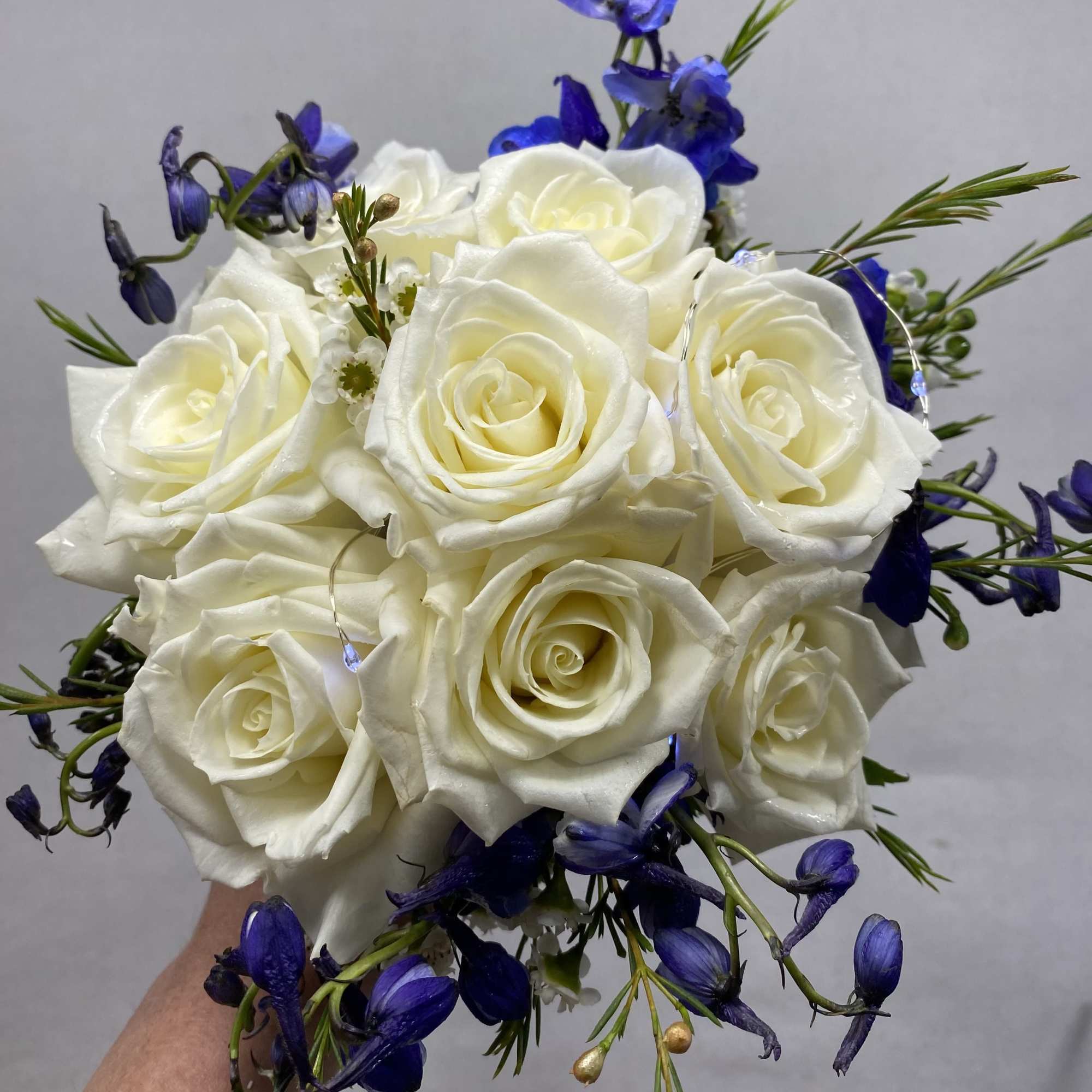 Handheld bouquet of white roses with blue flowers
