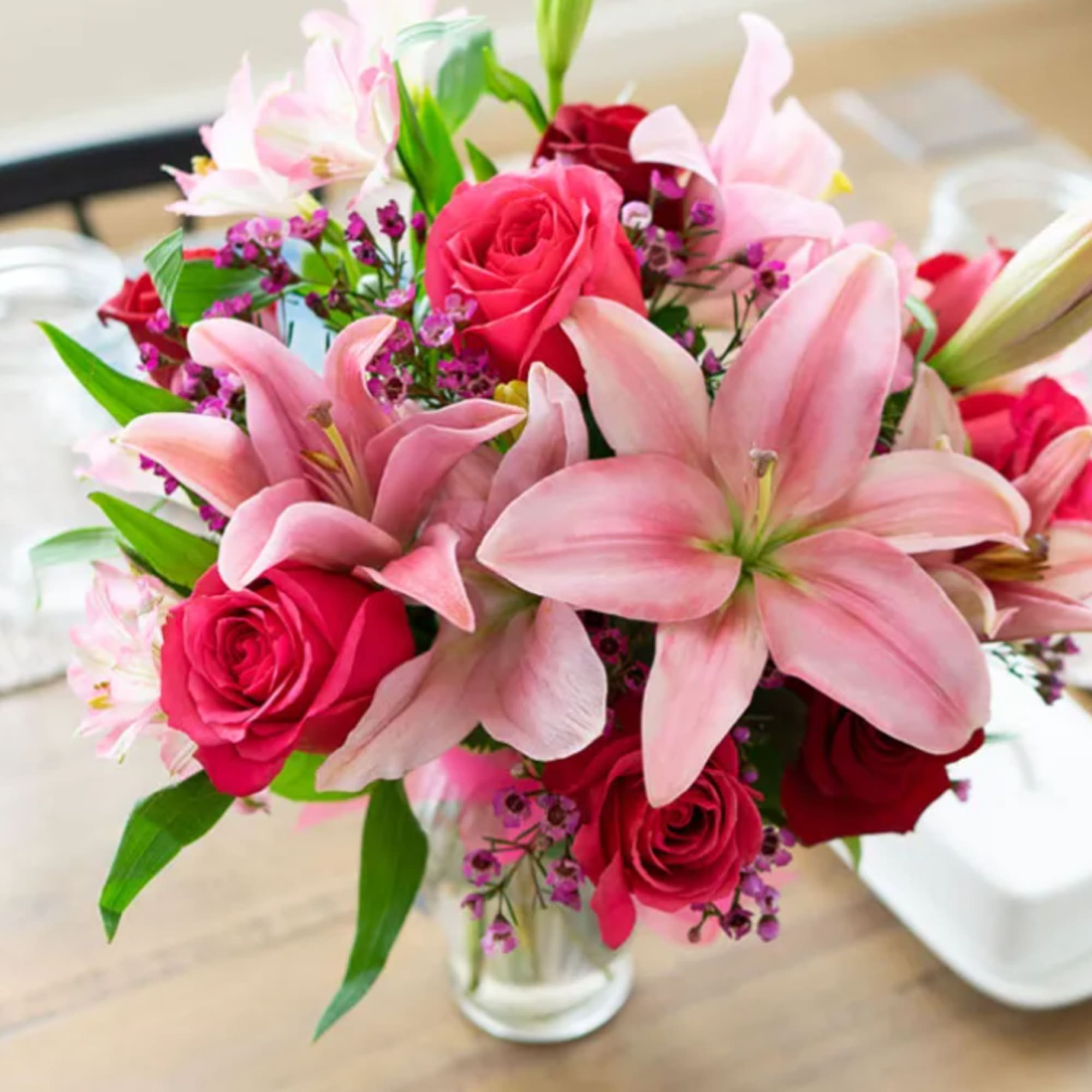 Pink lilies and red roses arranged in a clear glass vase
