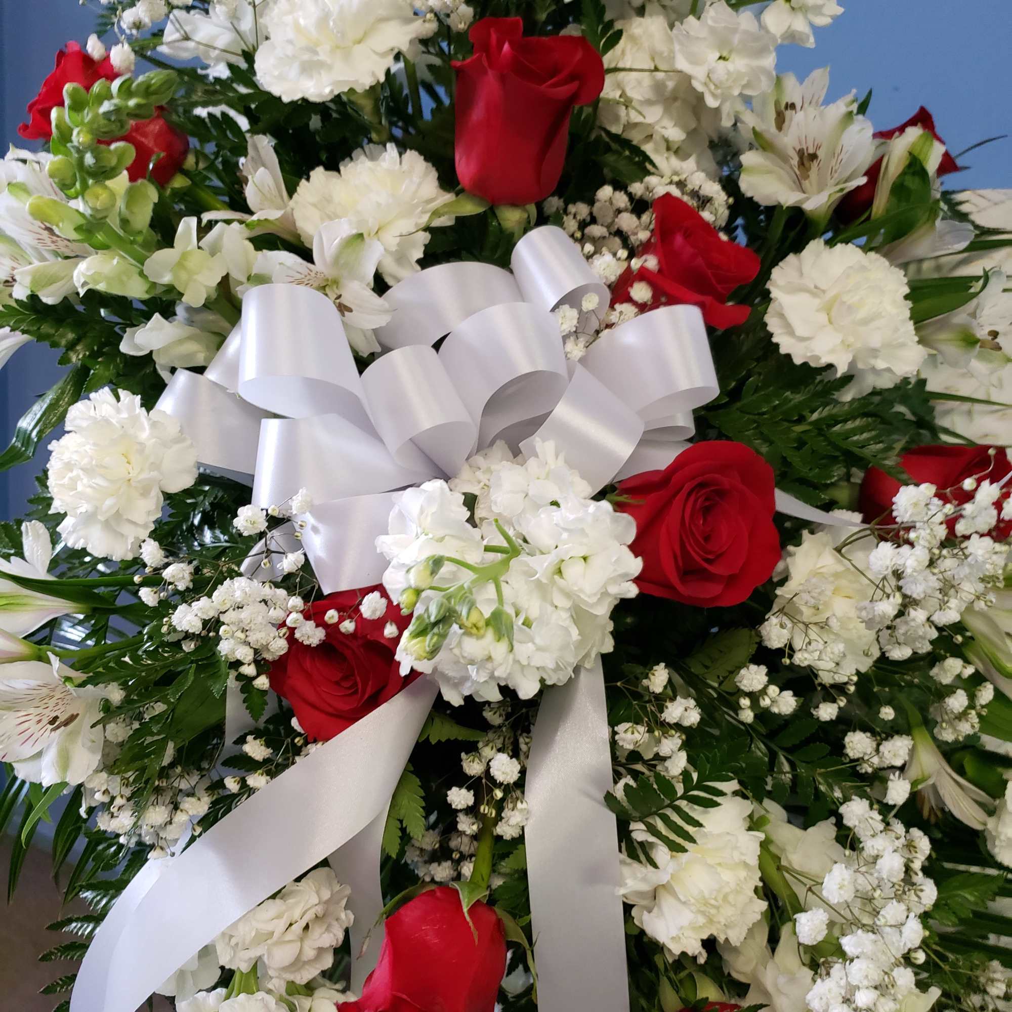 Red roses and white flowers arranged with a large white ribbon