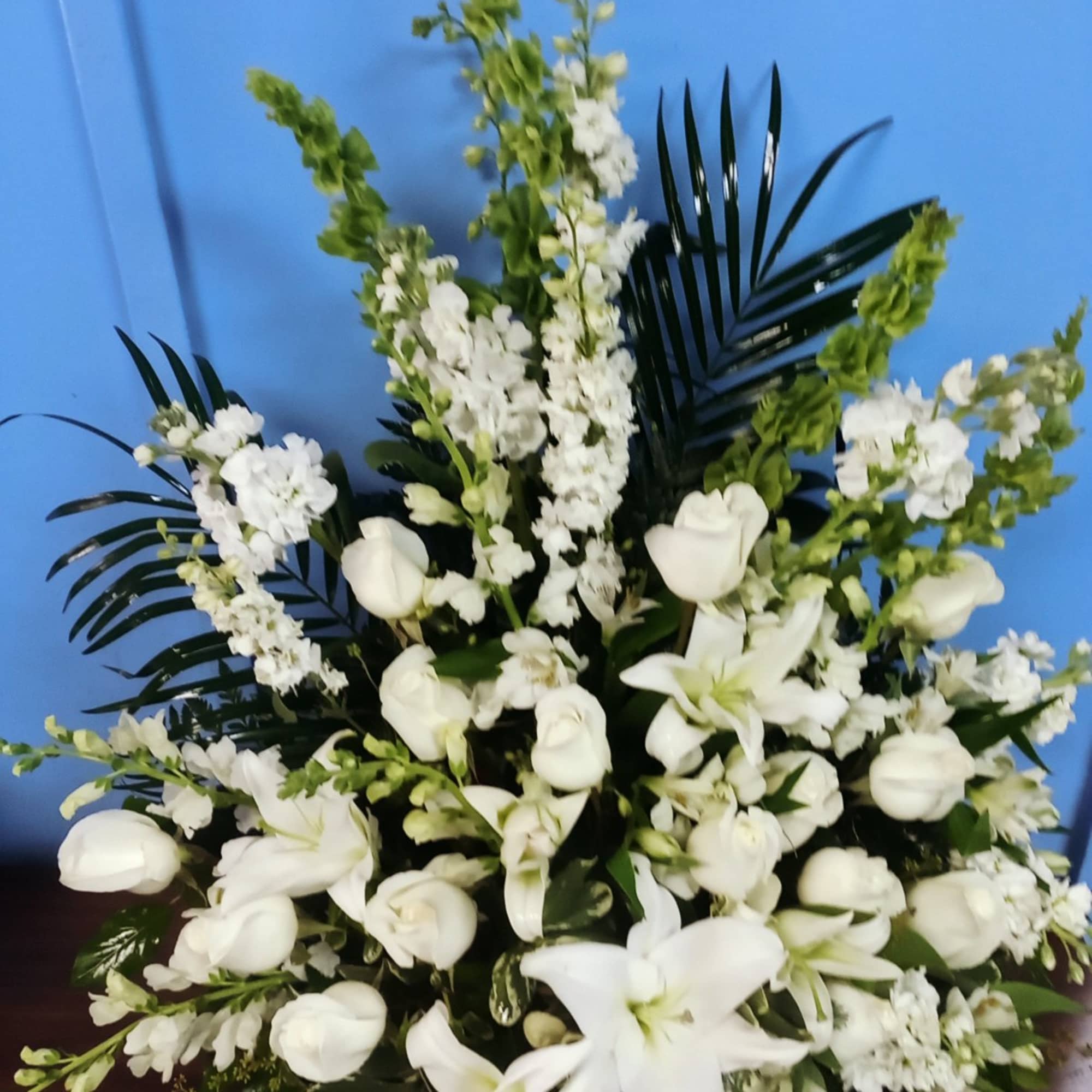 White lilies and roses arranged in a tall spray with dark palm fronds