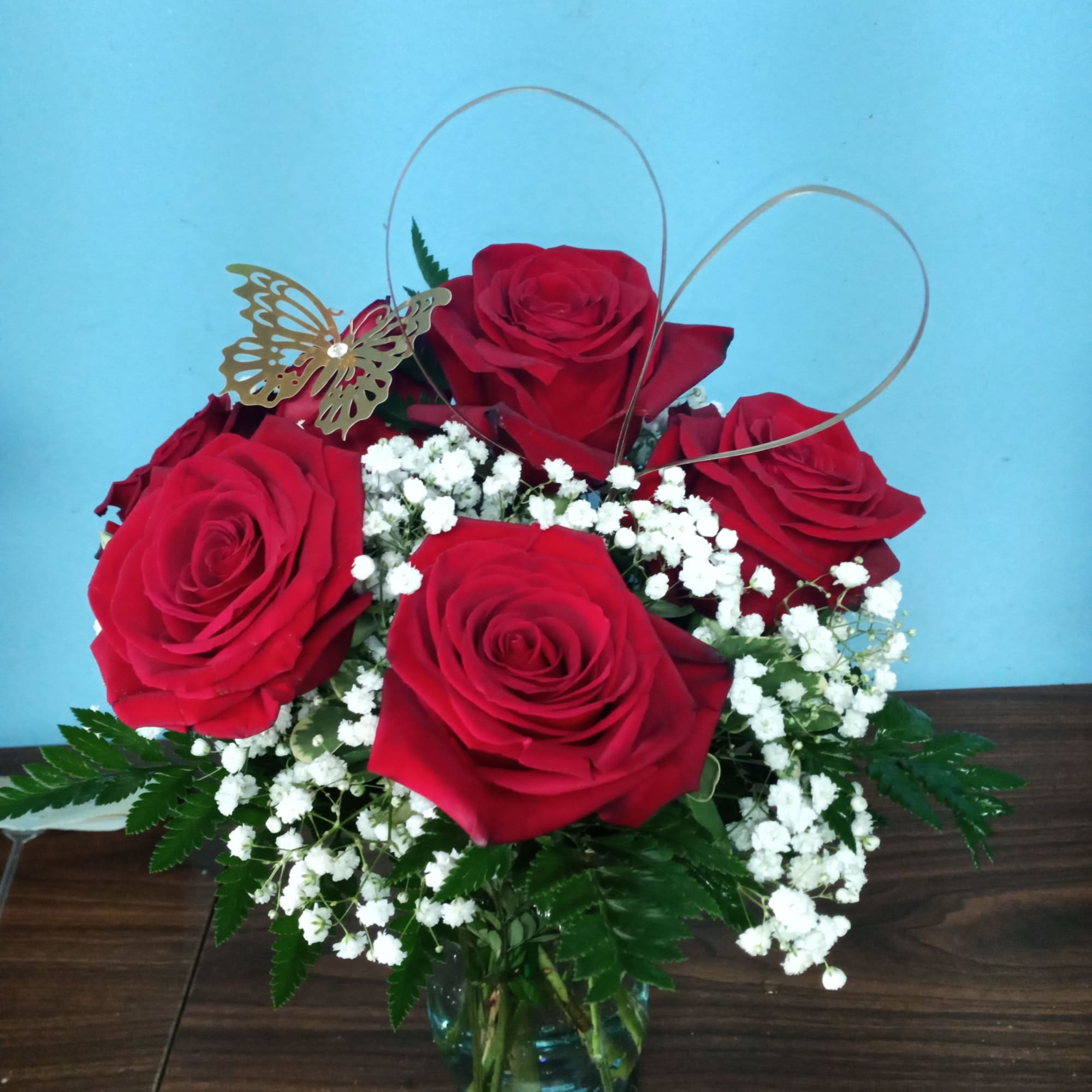 Red roses arranged in a glass vase with white baby's breath and a butterfly pick