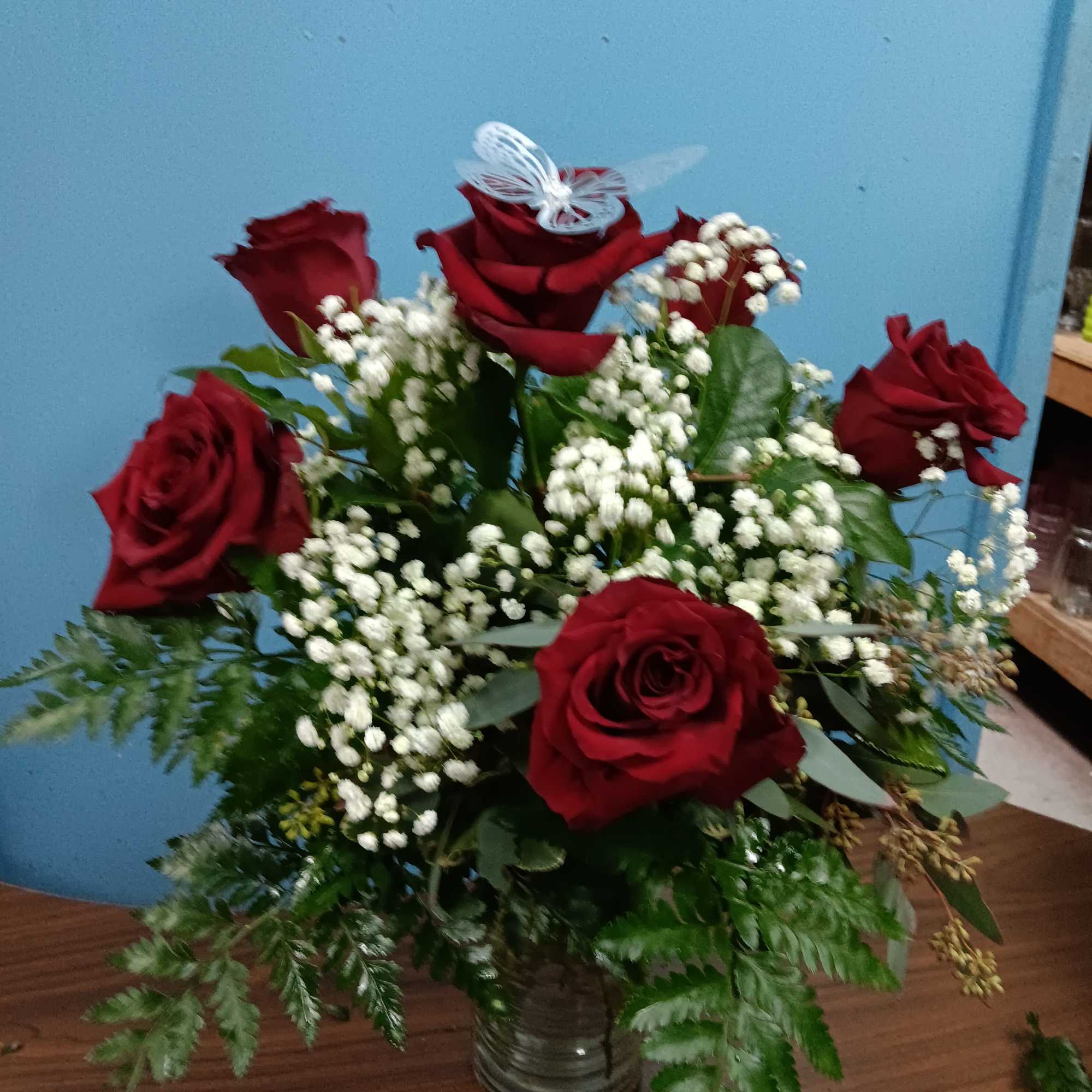 Red roses and white baby's breath in a glass vase with a butterfly topper