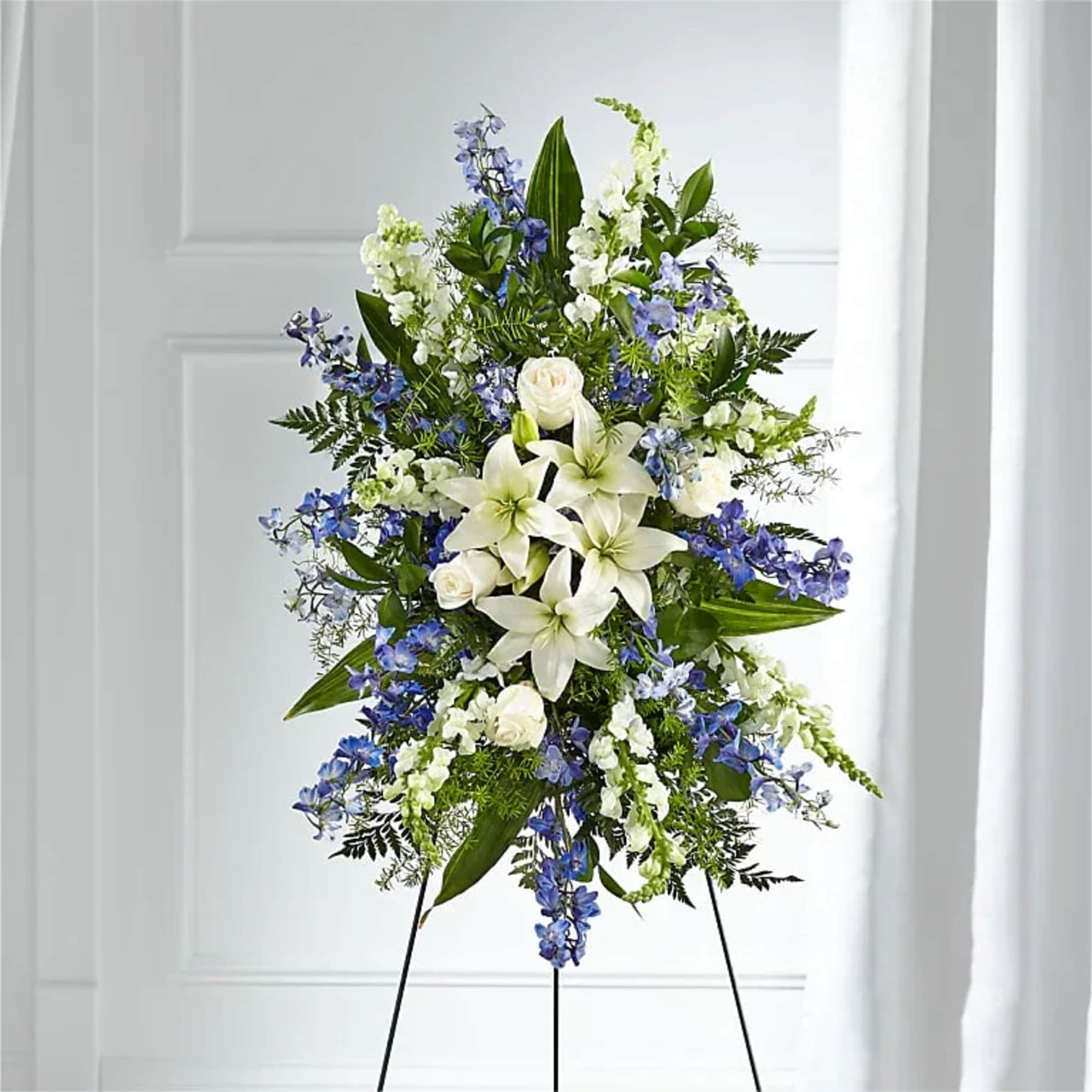 Standing floral spray with white lilies and blue flowers on a black easel