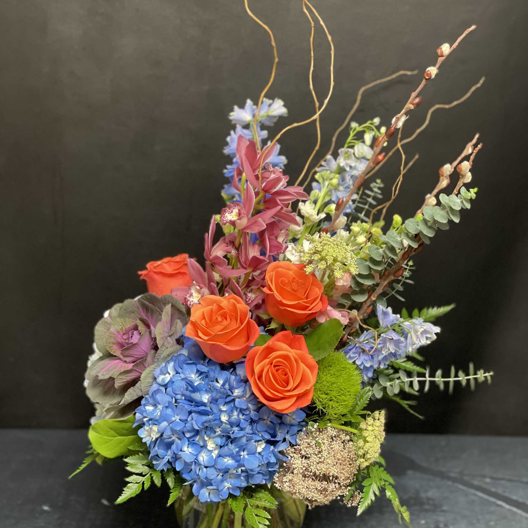 Colorful mixed bouquet in a glass vase with orange roses and blue hydrangea