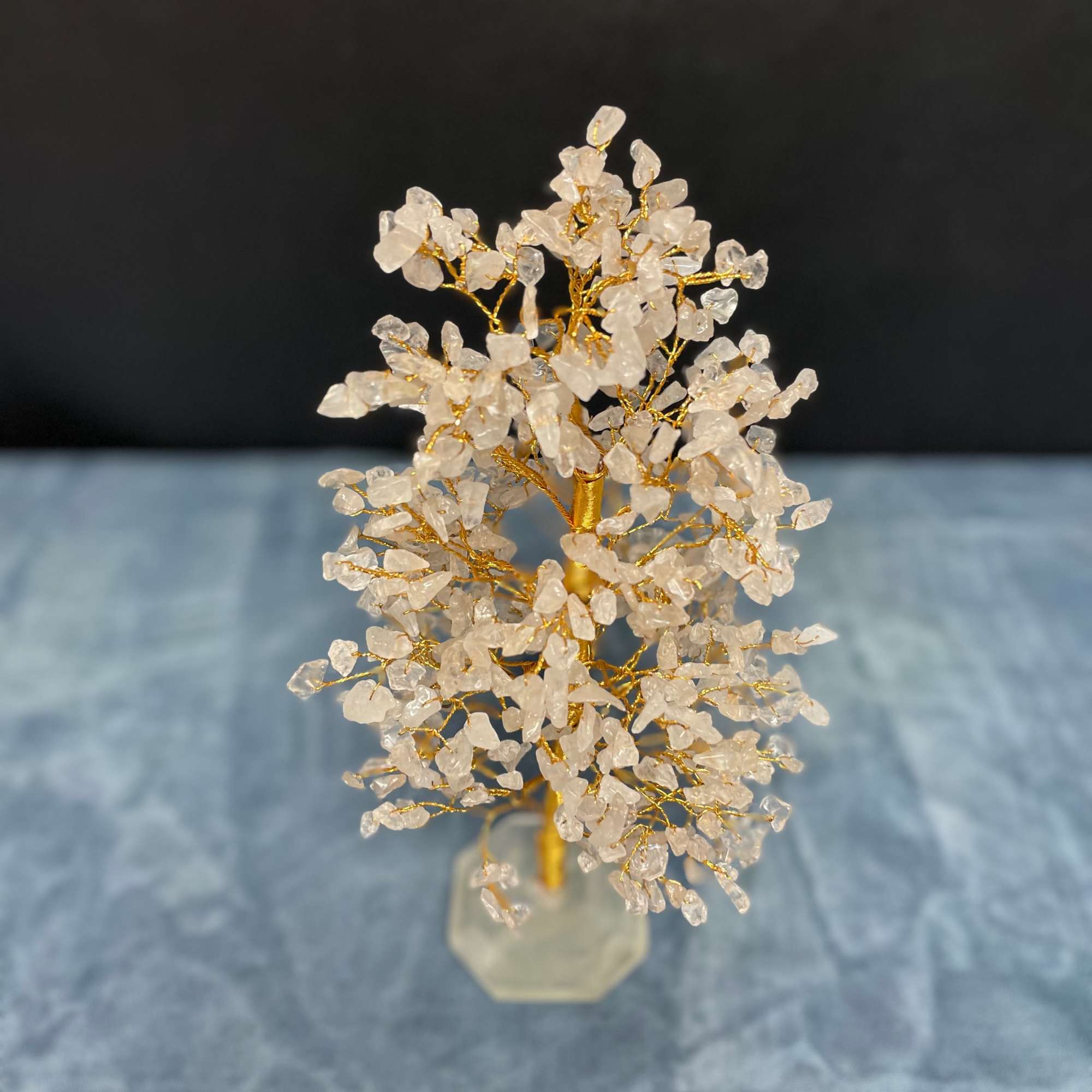 Small gold wire tree with clear crystal chips on a faceted clear base against a dark background