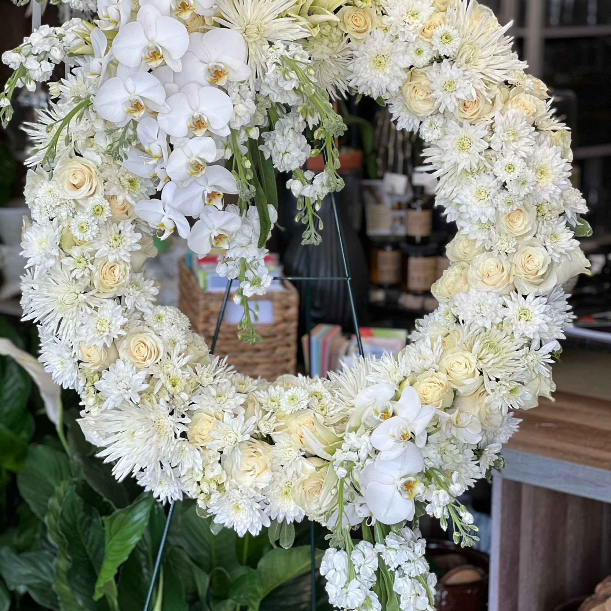 Large white and cream floral wreath with roses, orchids, and mums on a stand