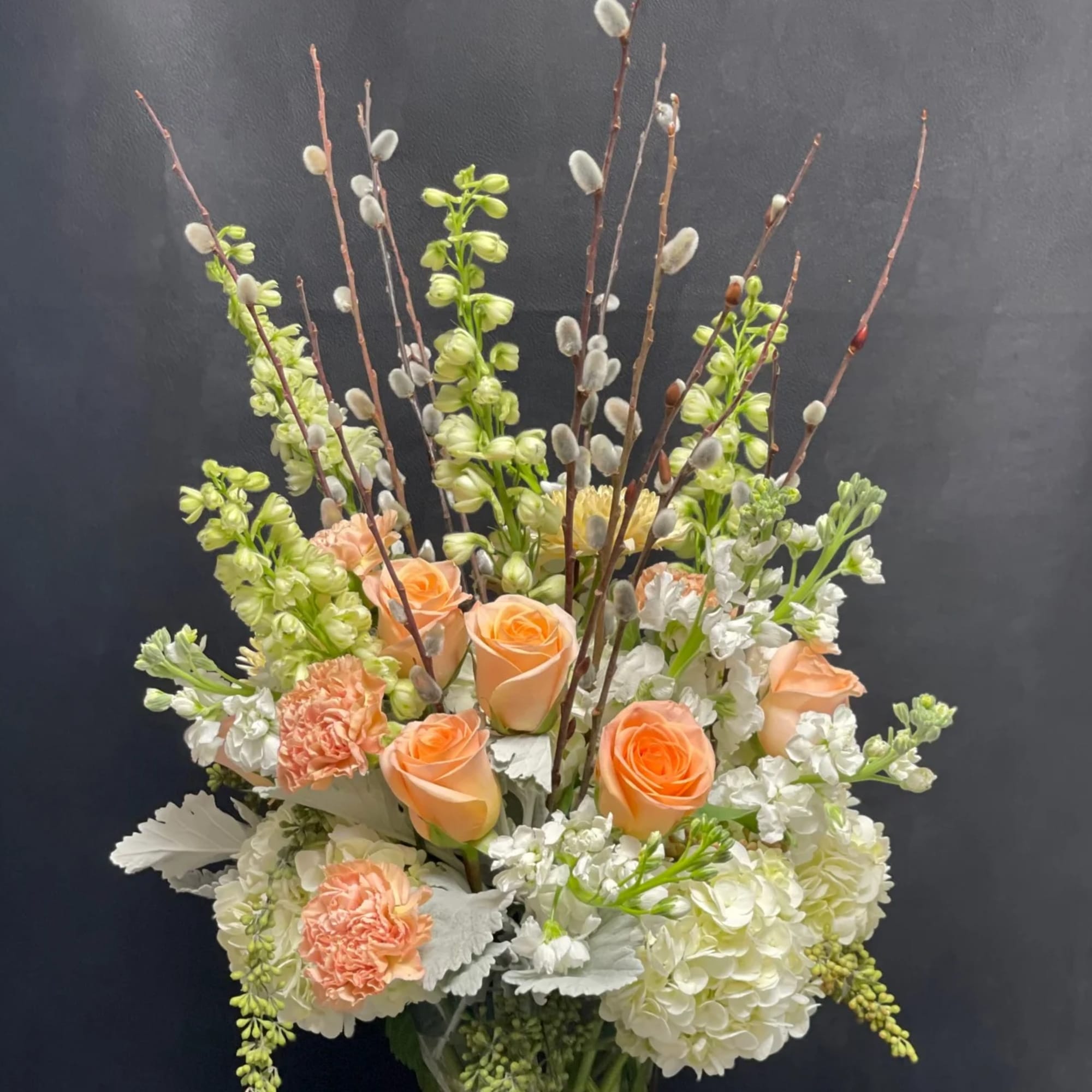 Tall peach and white flower arrangement with roses and carnations in a clear glass vase