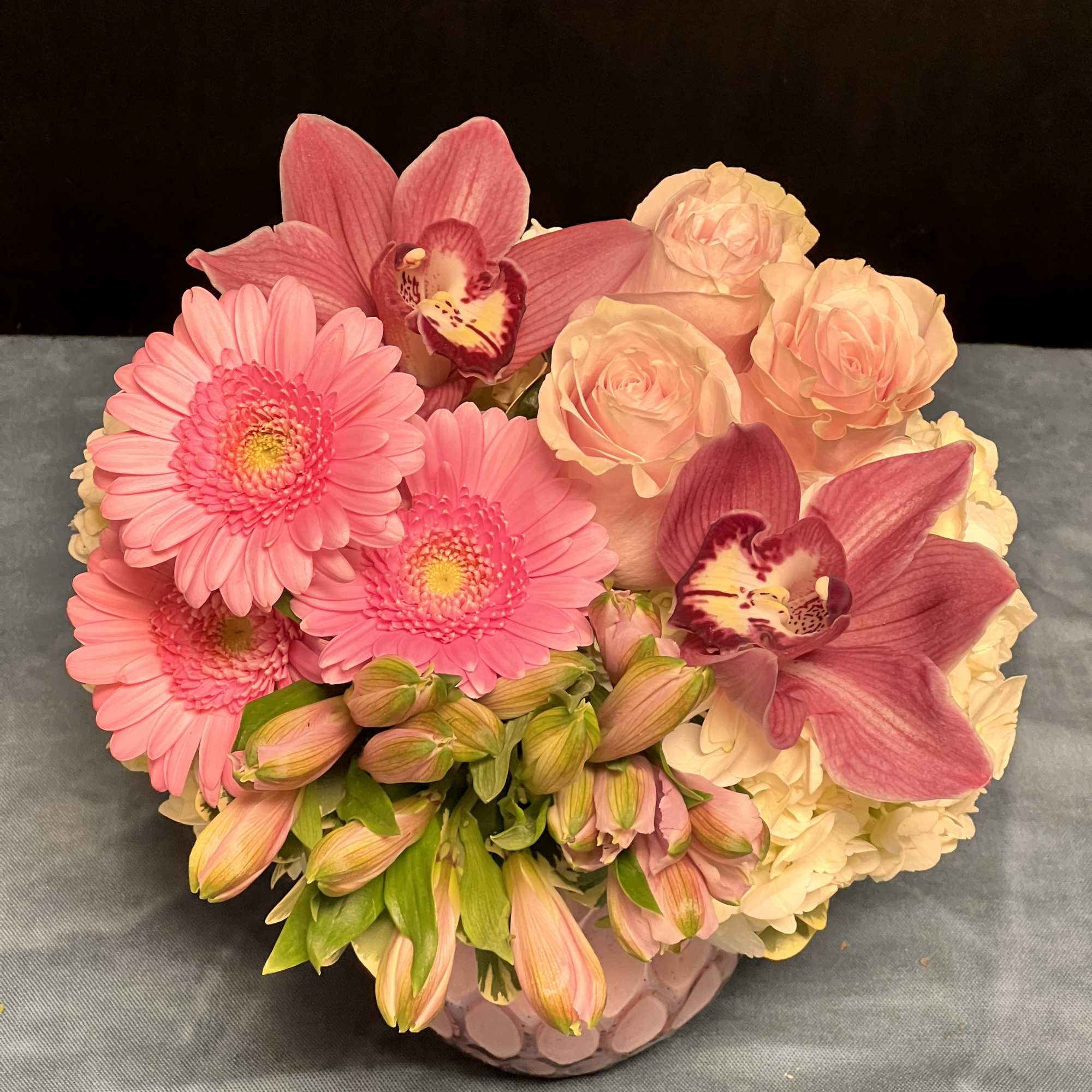 Low pink arrangement with gerbera daisies, roses, orchids, and white hydrangeas in a round vase