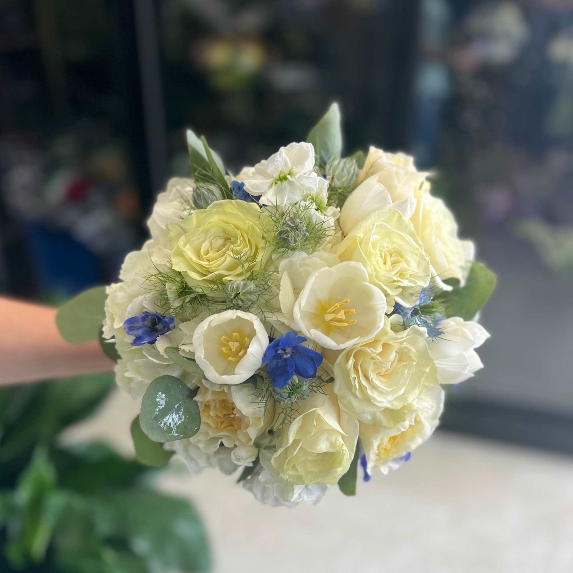 Hand-tied bouquet of pale yellow roses, white blooms, and bright blue accent flowers