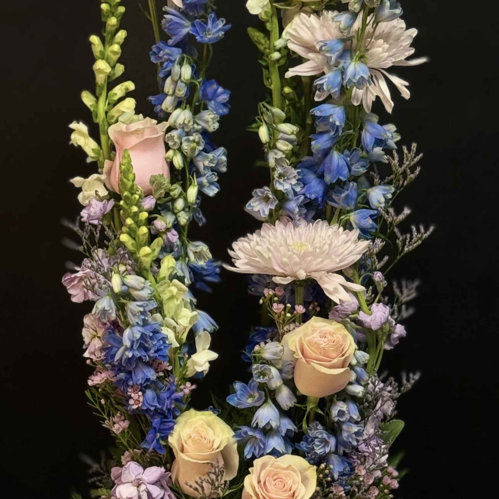 Tall pastel arrangement with peach roses, blue delphinium, and white mums in a round bowl vase