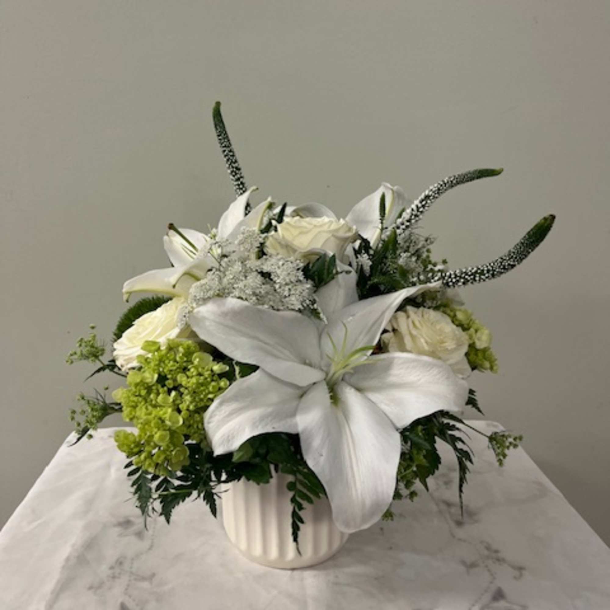 White lilies and roses arranged in a white vase