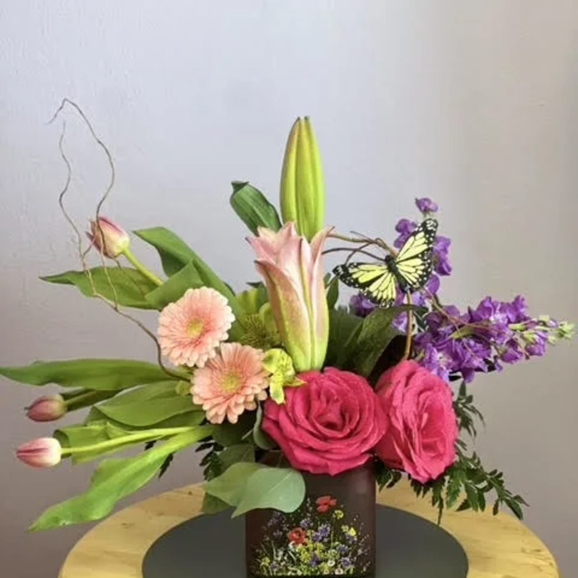 Pink roses and lilies in a square vase with a butterfly accent