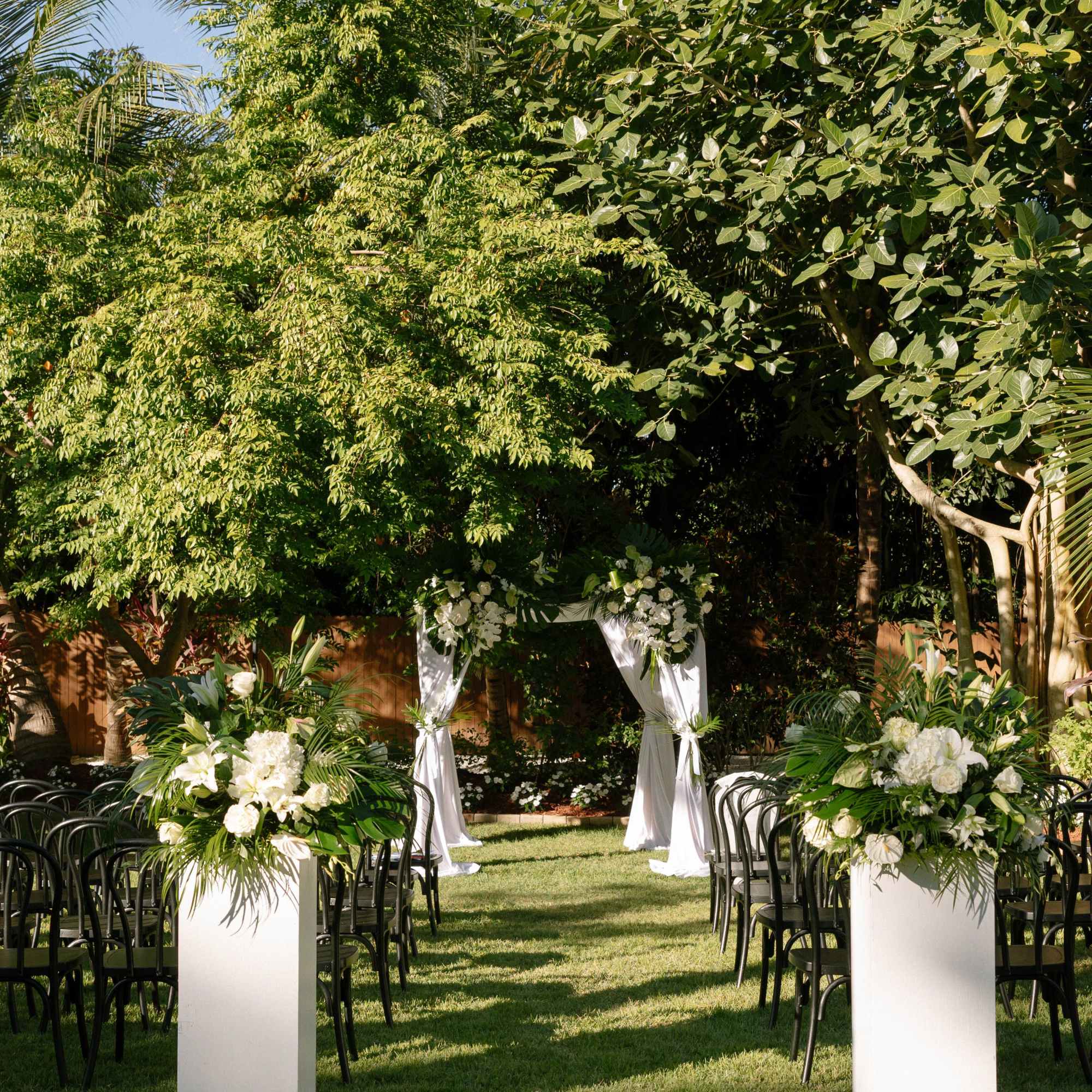Outdoor wedding aisle with white floral arrangements and a draped arch