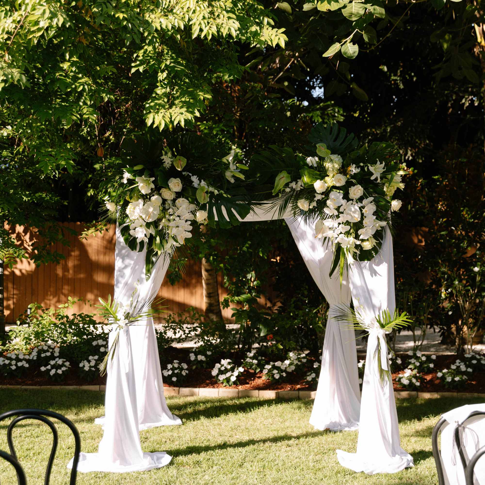 White floral wedding arch draped with fabric in a garden setting