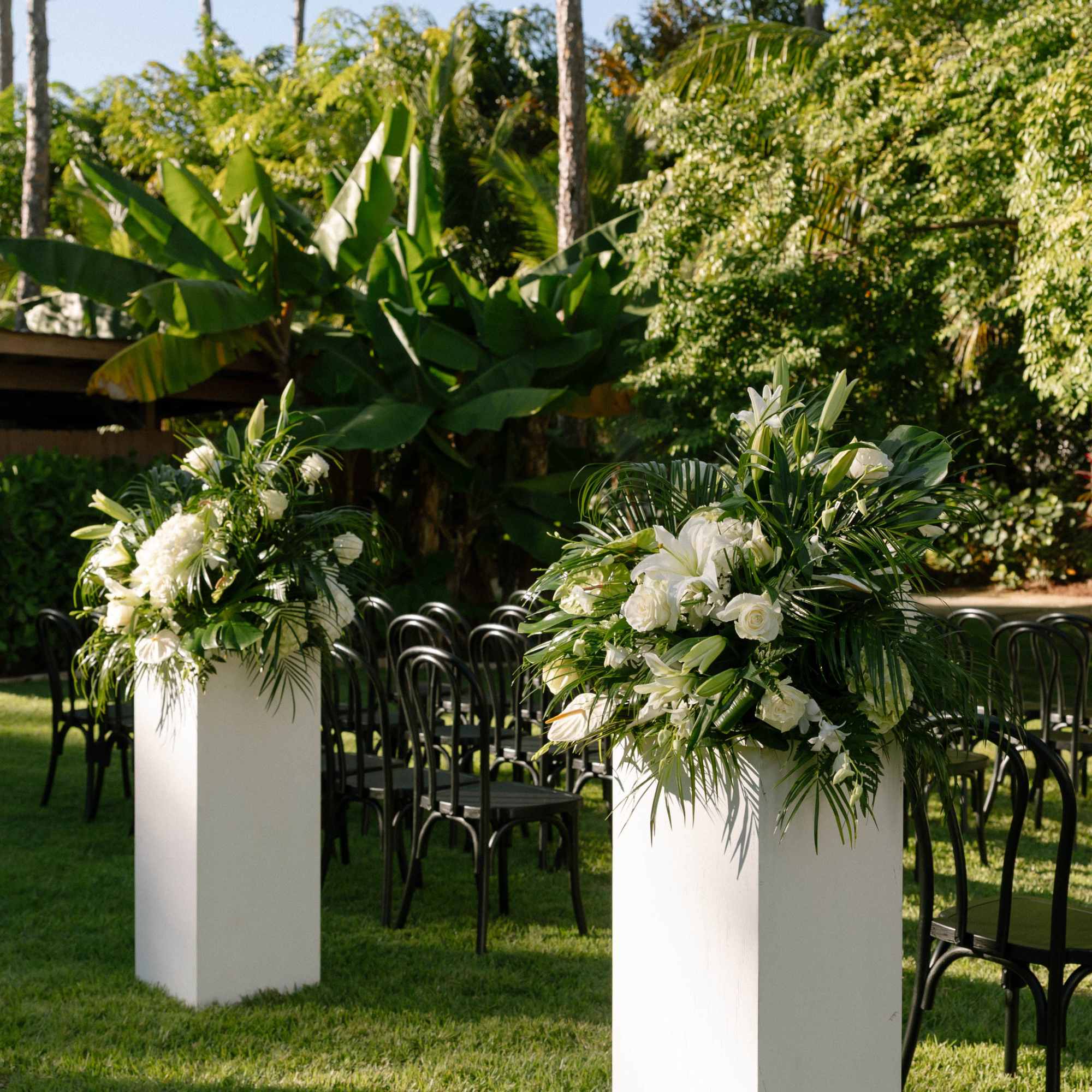 White floral arrangements on tall pedestals at an outdoor ceremony