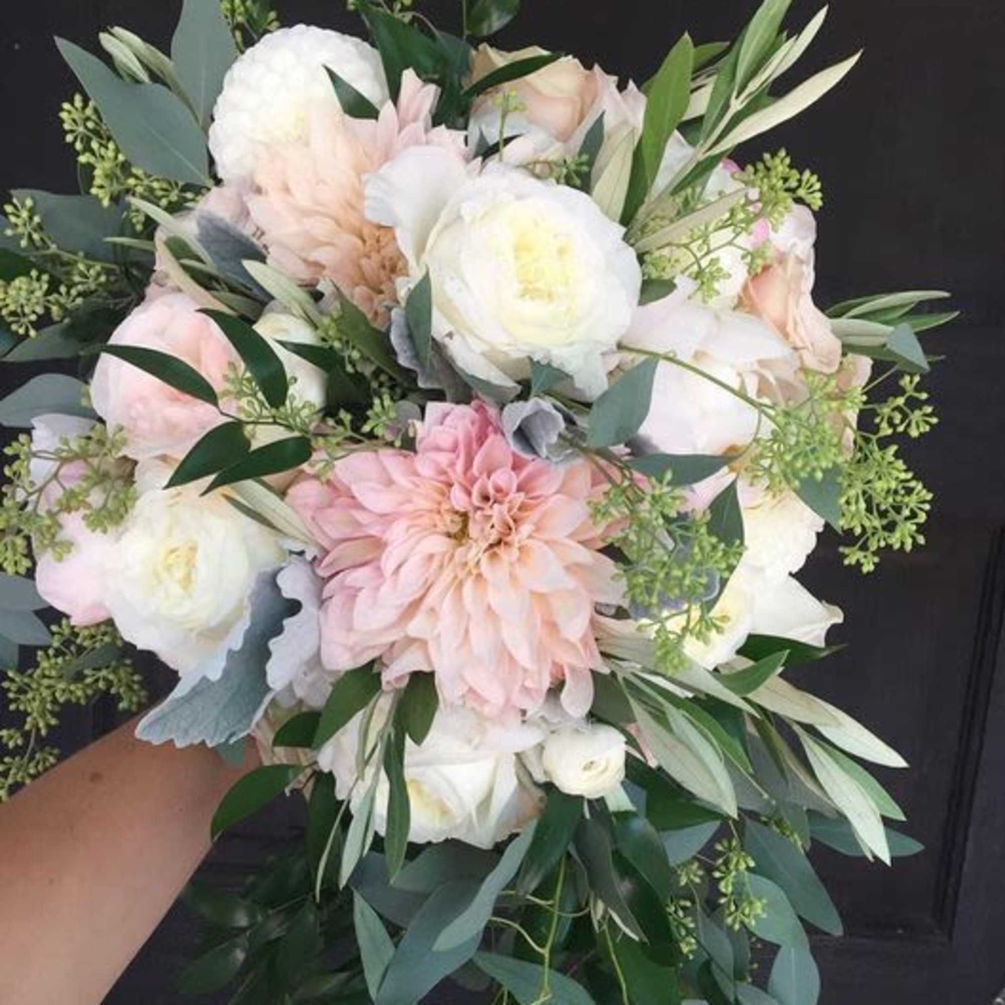 Handheld bouquet of pale pink and white flowers with greenery