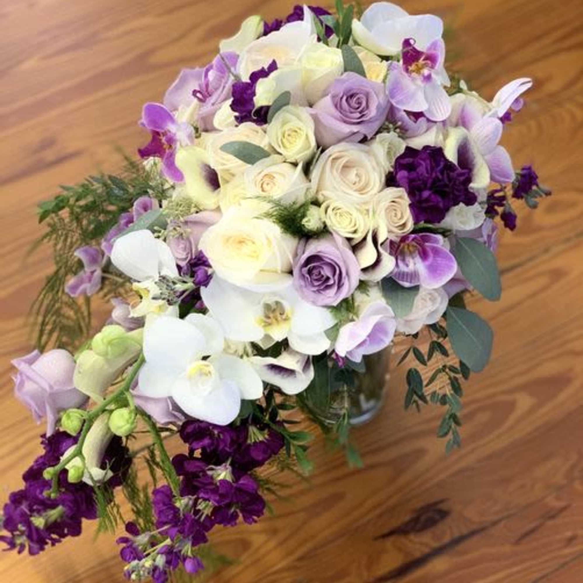 Bouquet of white and lavender roses with purple orchids in a glass vase