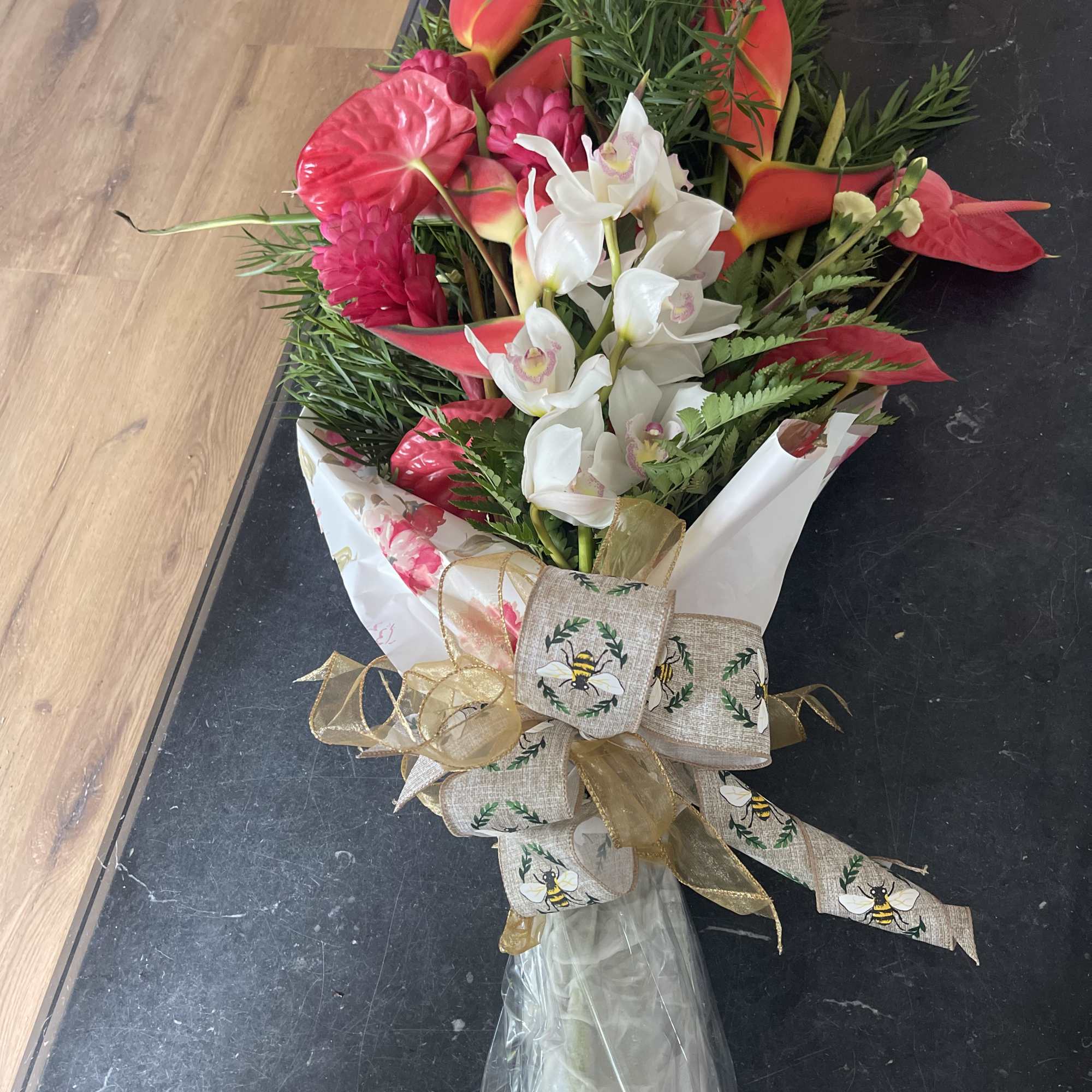 Bouquet of white orchids, red anthuriums, and pink tropical flowers with a decorative ribbon