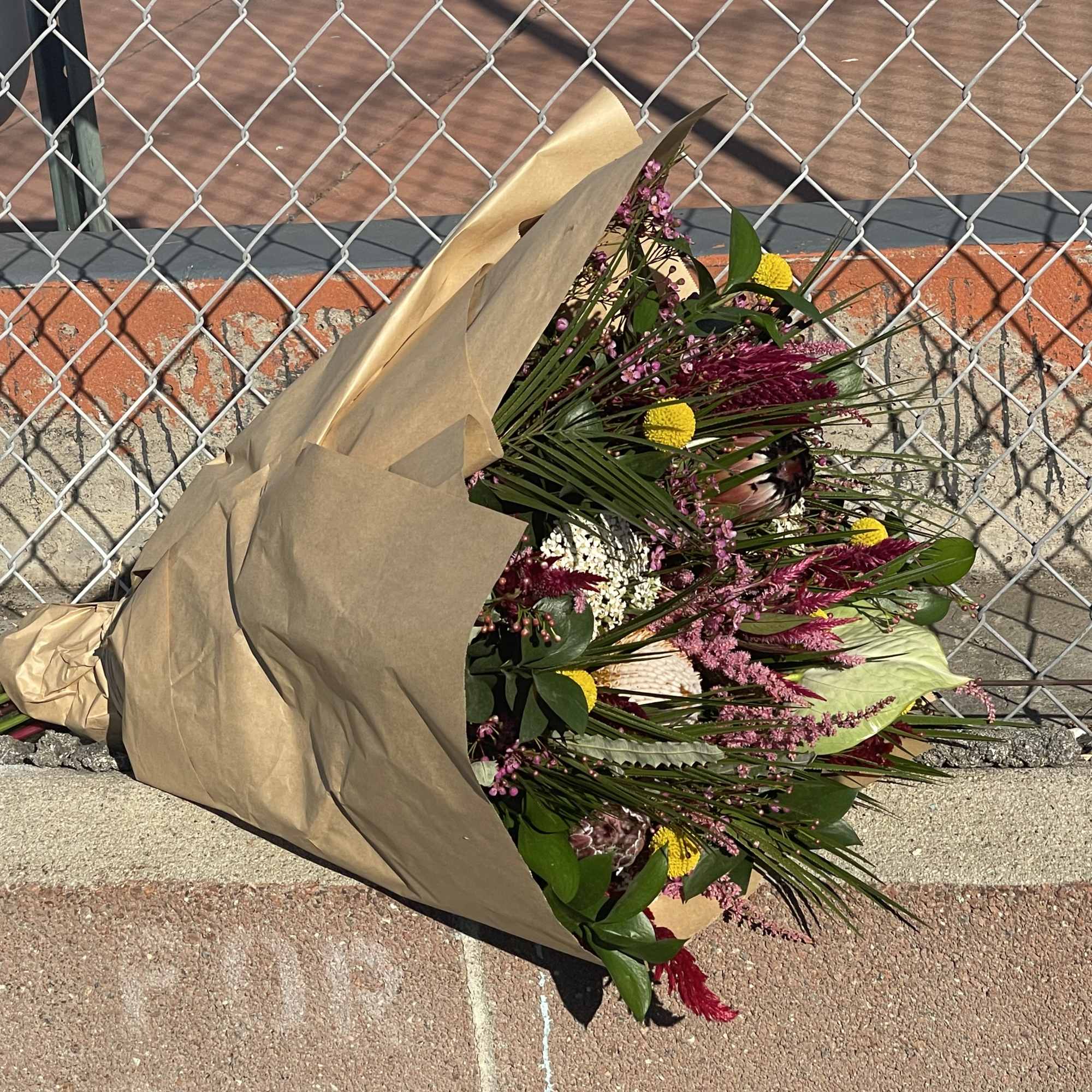 Wrapped bouquet with pink and yellow flowers on a curb