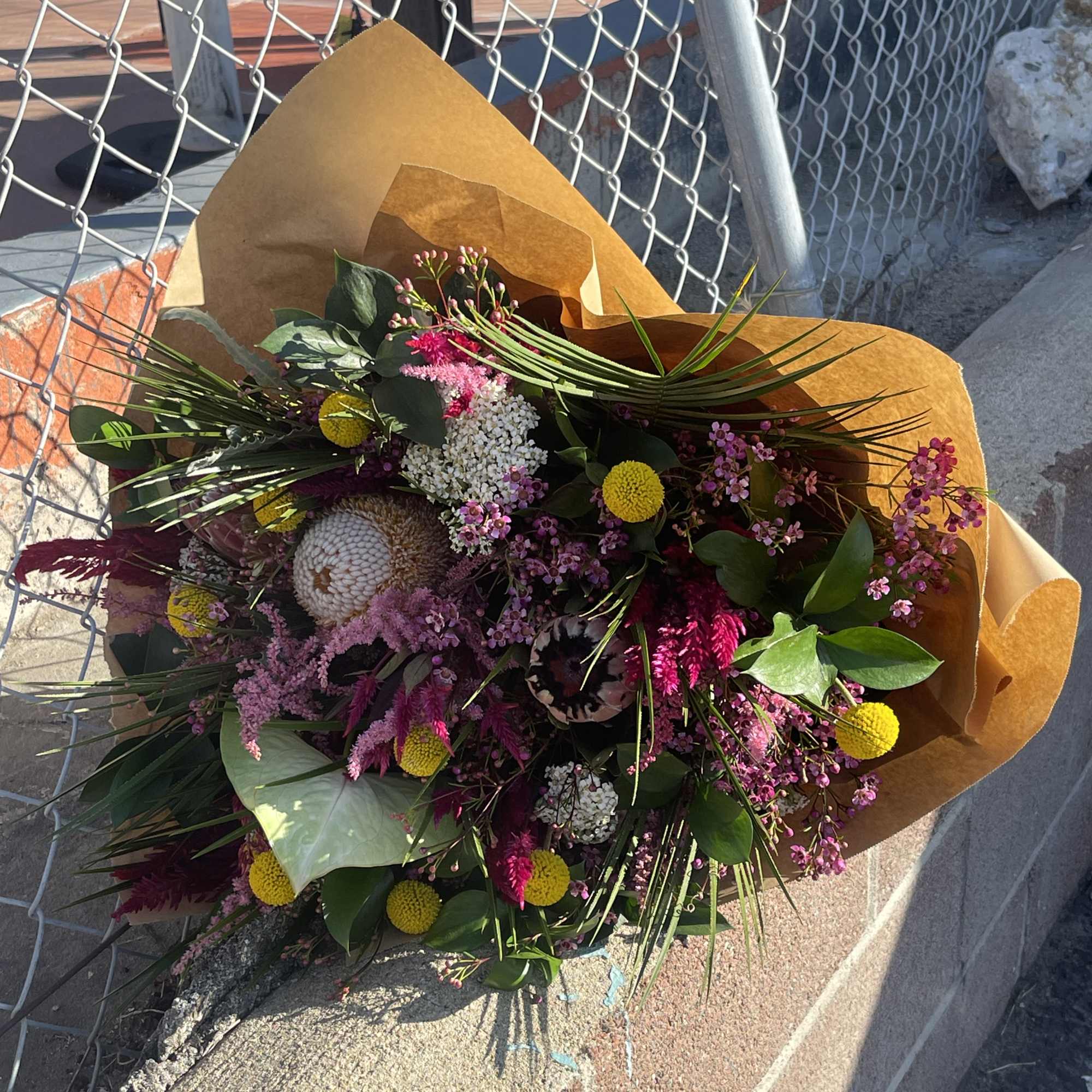 Mixed bouquet with pink, yellow, and white flowers wrapped in brown paper