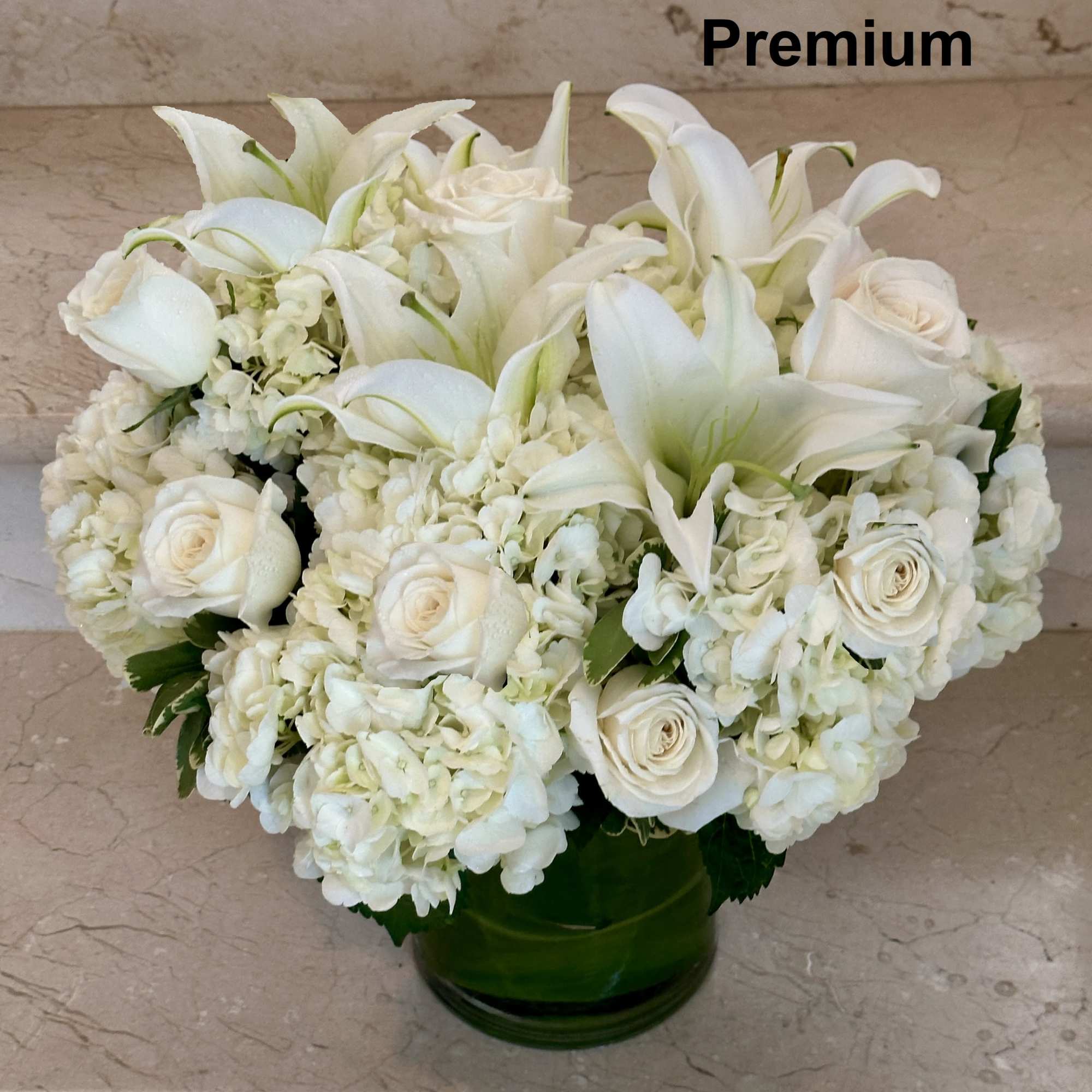 Low round arrangement of white lilies, roses, and hydrangeas in a clear glass vase
