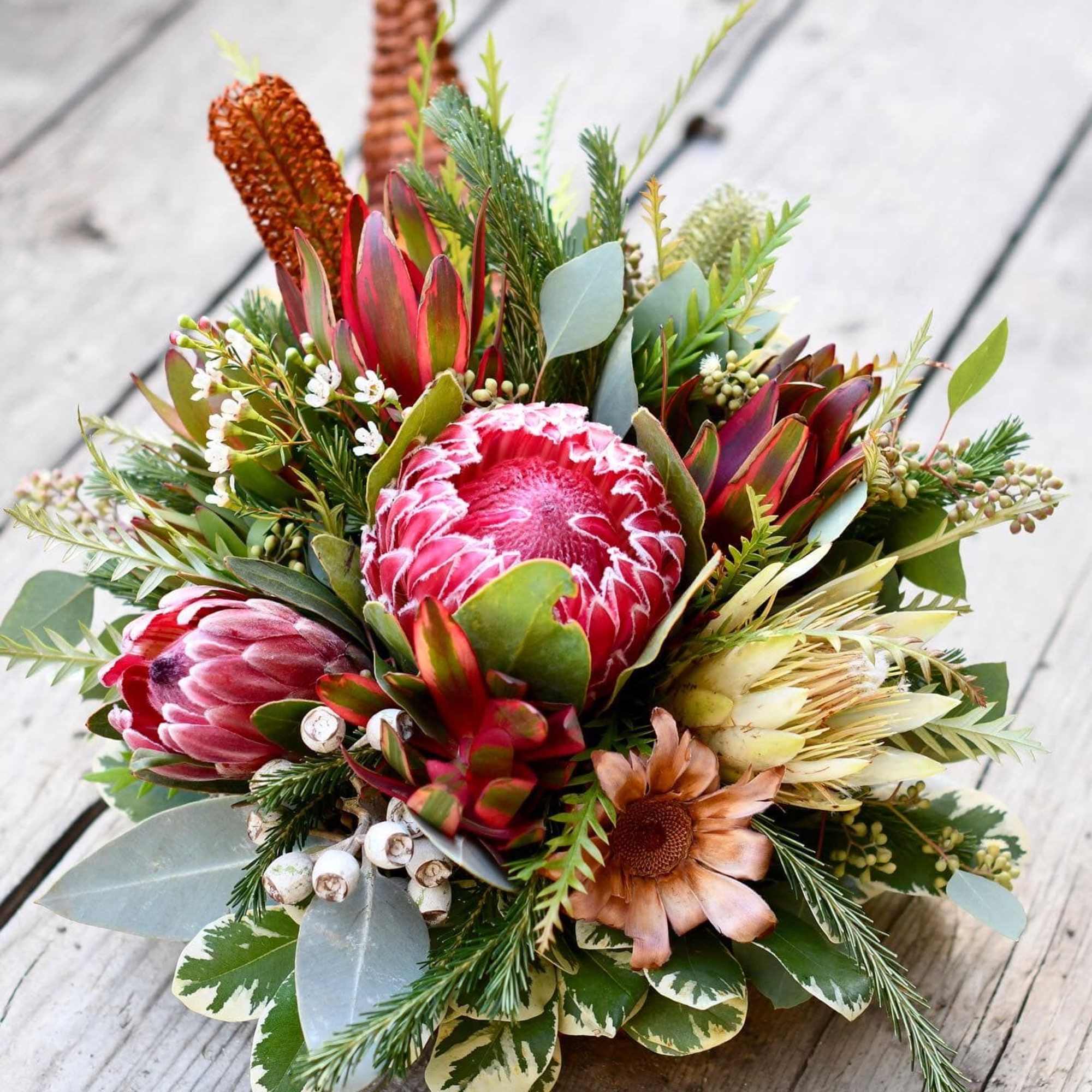 Bouquet of pink protea and mixed greenery on a wooden surface