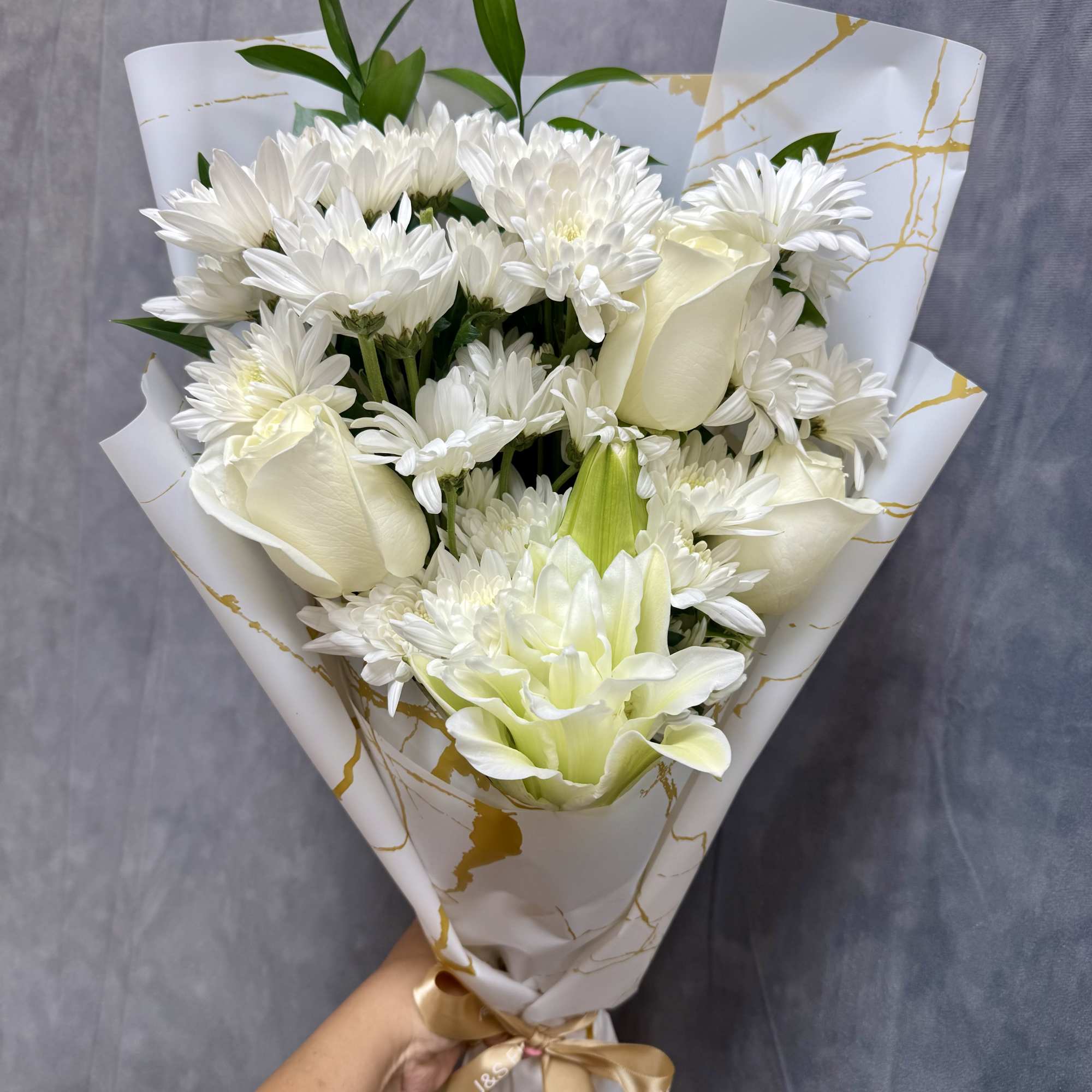White bouquet with daisies, roses, and a lily wrapped in patterned paper