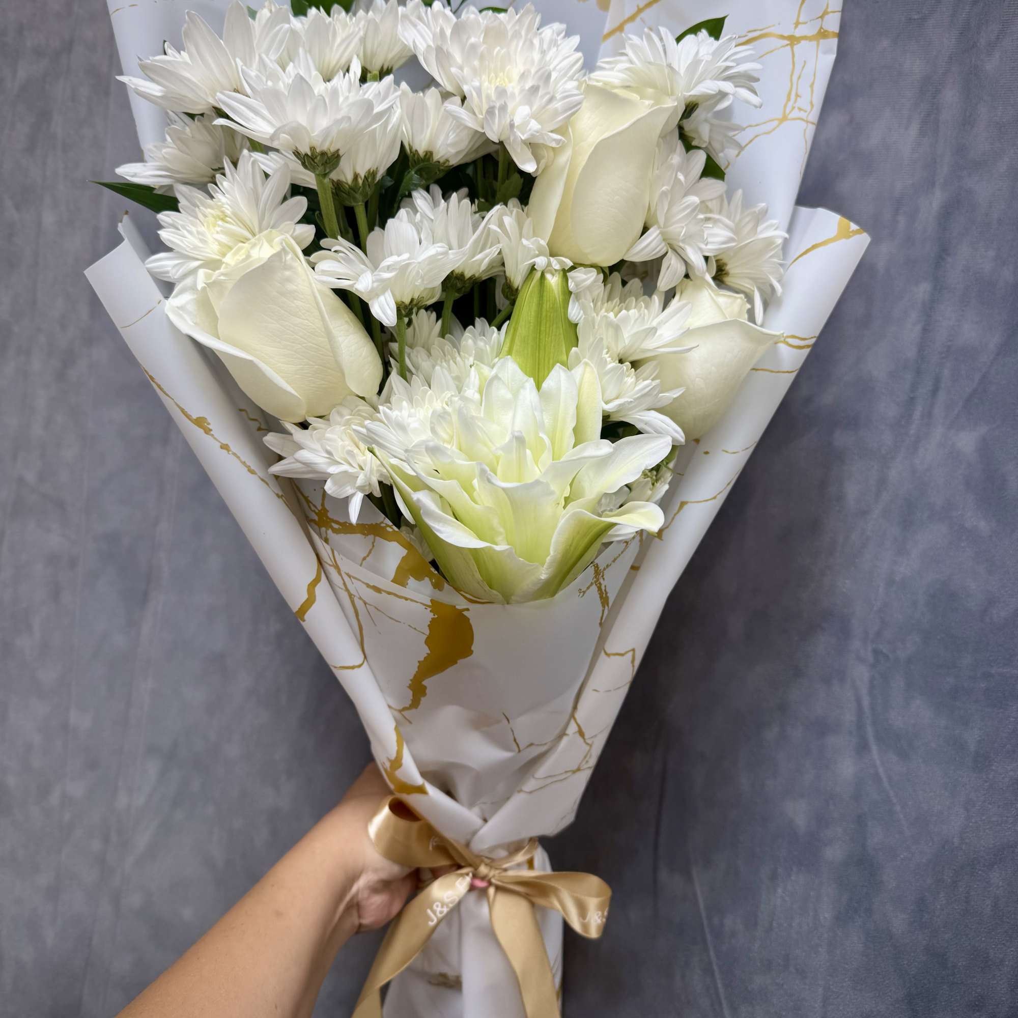 White bouquet of daisies and roses wrapped in gold-accented paper
