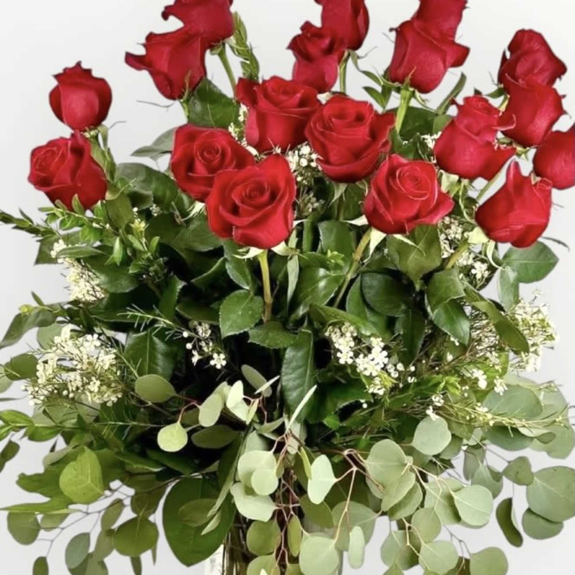 Tall arrangement of red roses with eucalyptus and white filler blooms in a clear glass vase