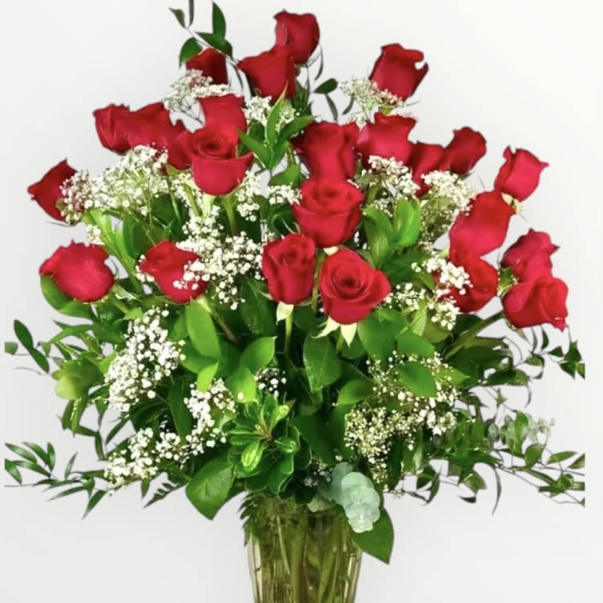 Tall arrangement of long-stem red roses with white filler flowers in a clear glass vase