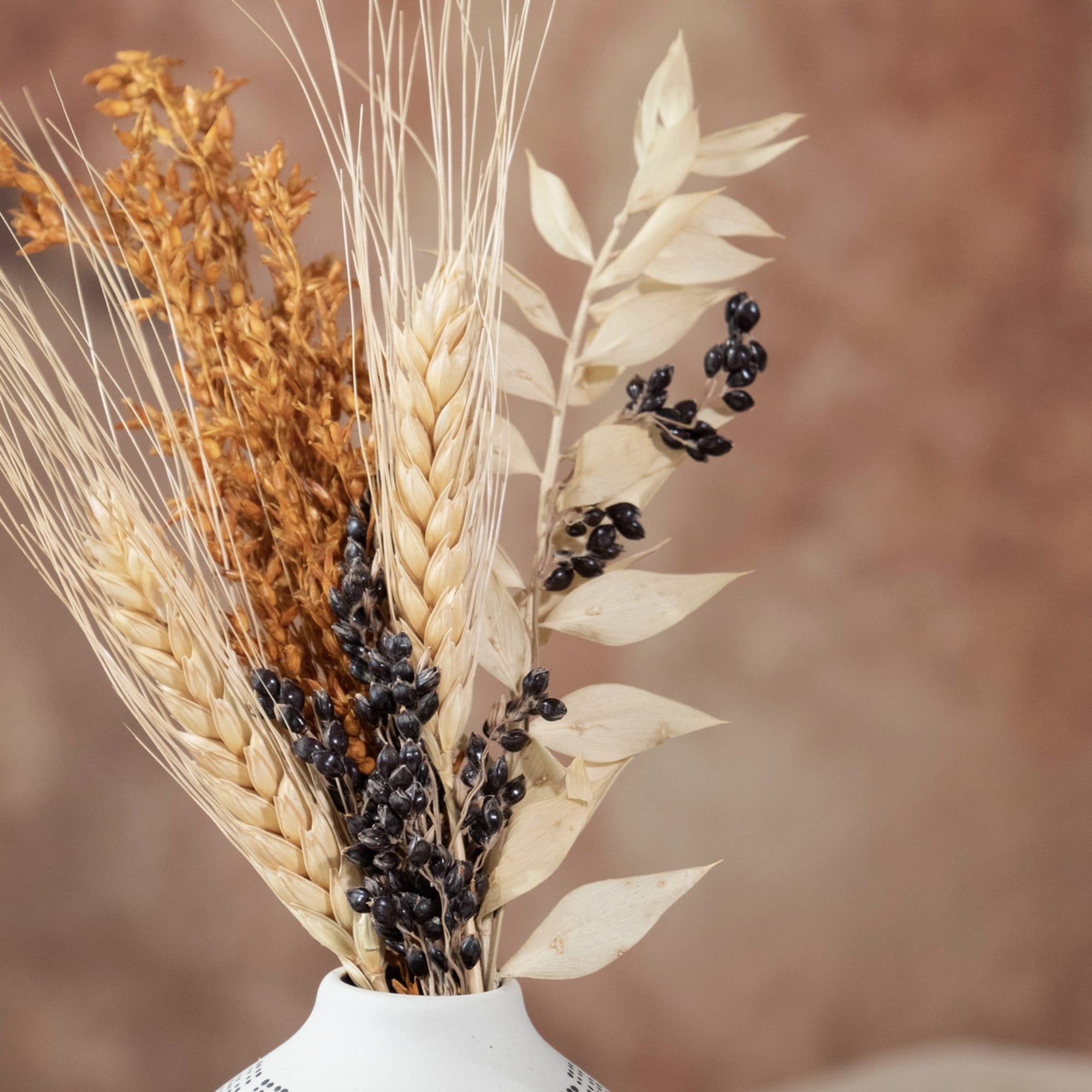 Dried wheat and seed stems in a white vase